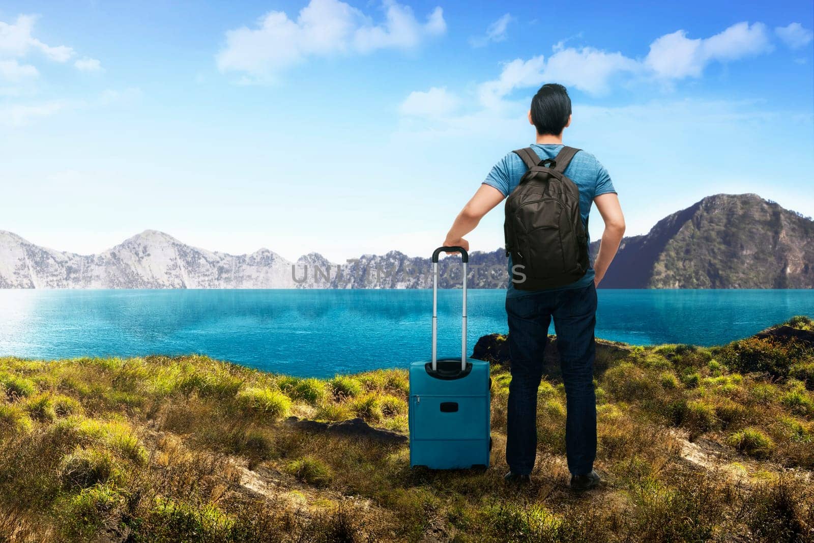 Back view of asian traveler man with suitcase enjoying lake view at mountain