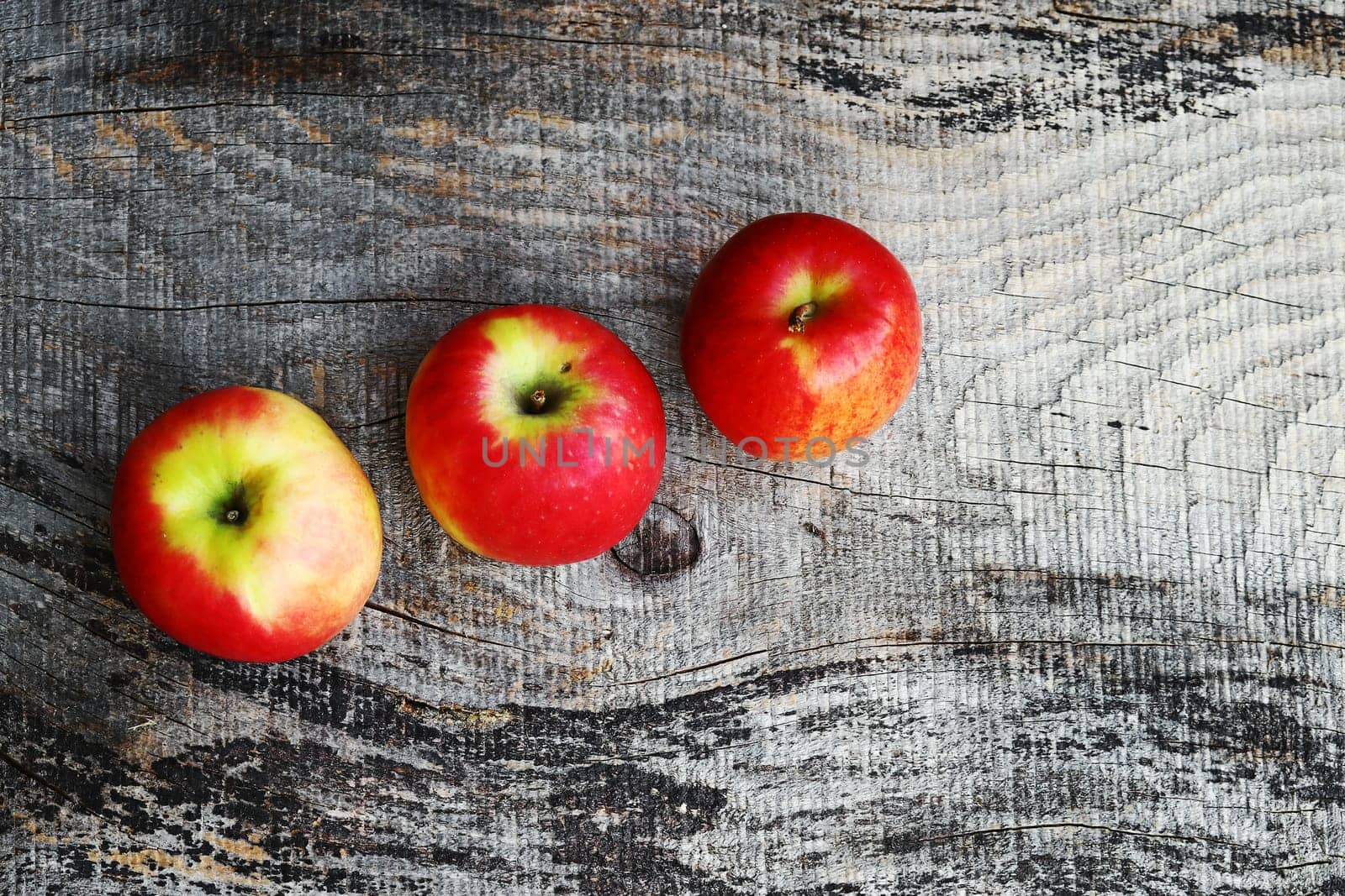 Three red fresh apples on a wooden surface