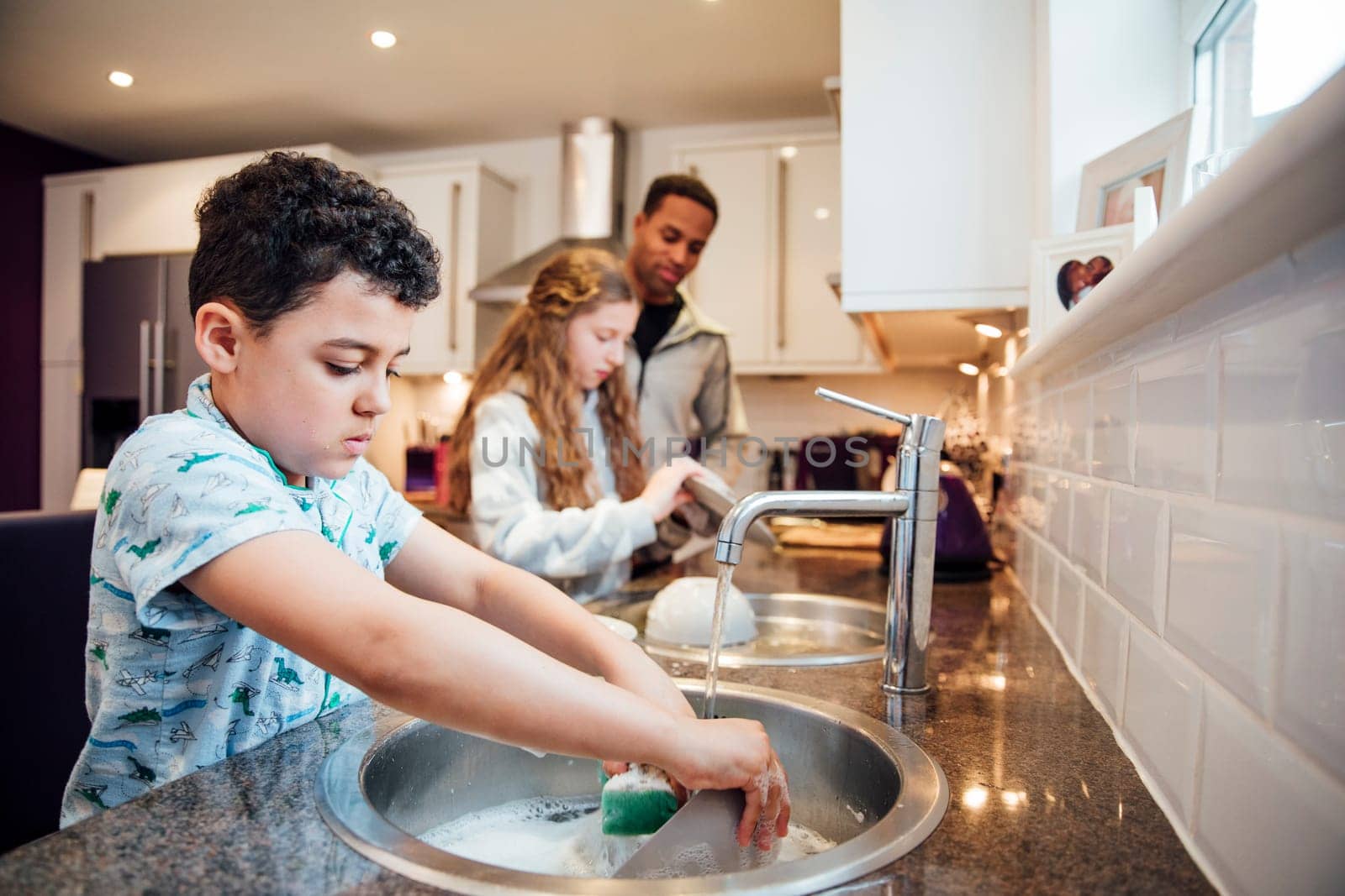 Little boy and his sister are helping dad with the washing up at home.
