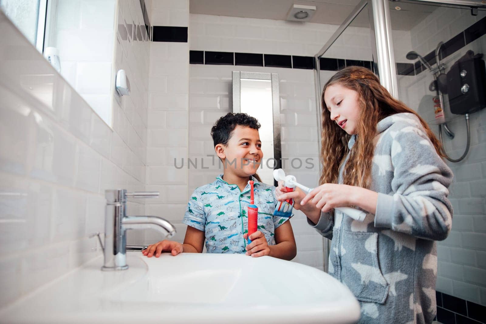 Little boy and his older sister are brushing their teeth together in the bathroom at home.