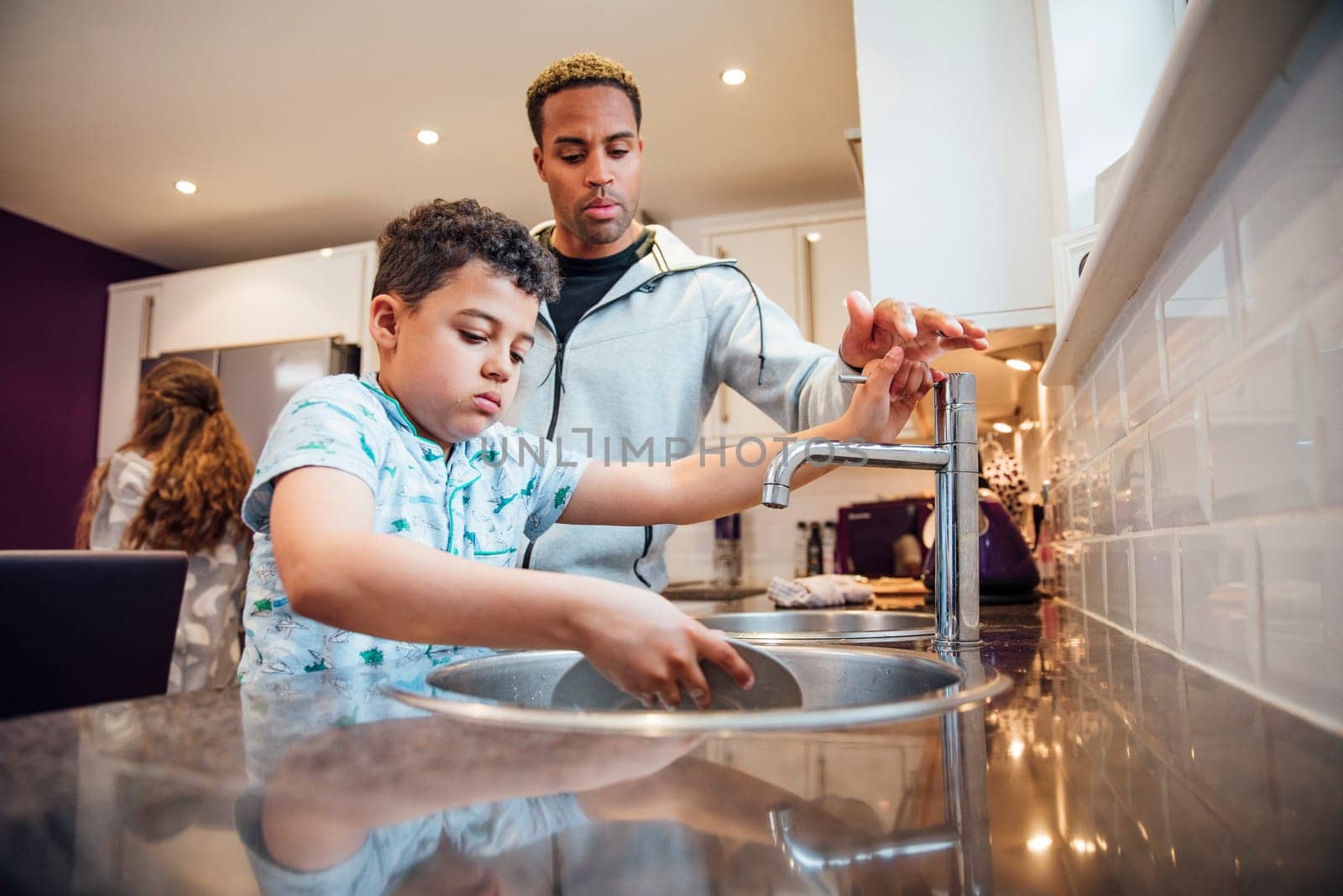 Little boy and his father are washing the dishes together at home.