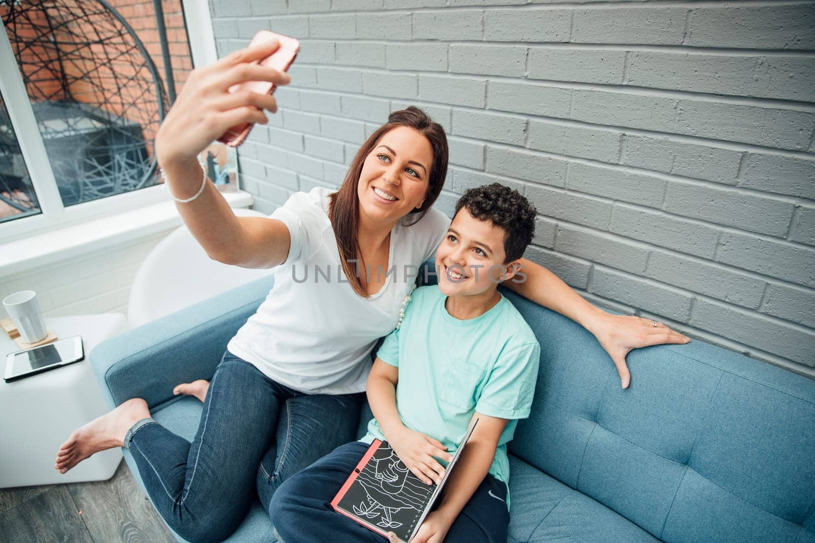 Mother and her son are taking a selfie while reading in the conservatory at home.