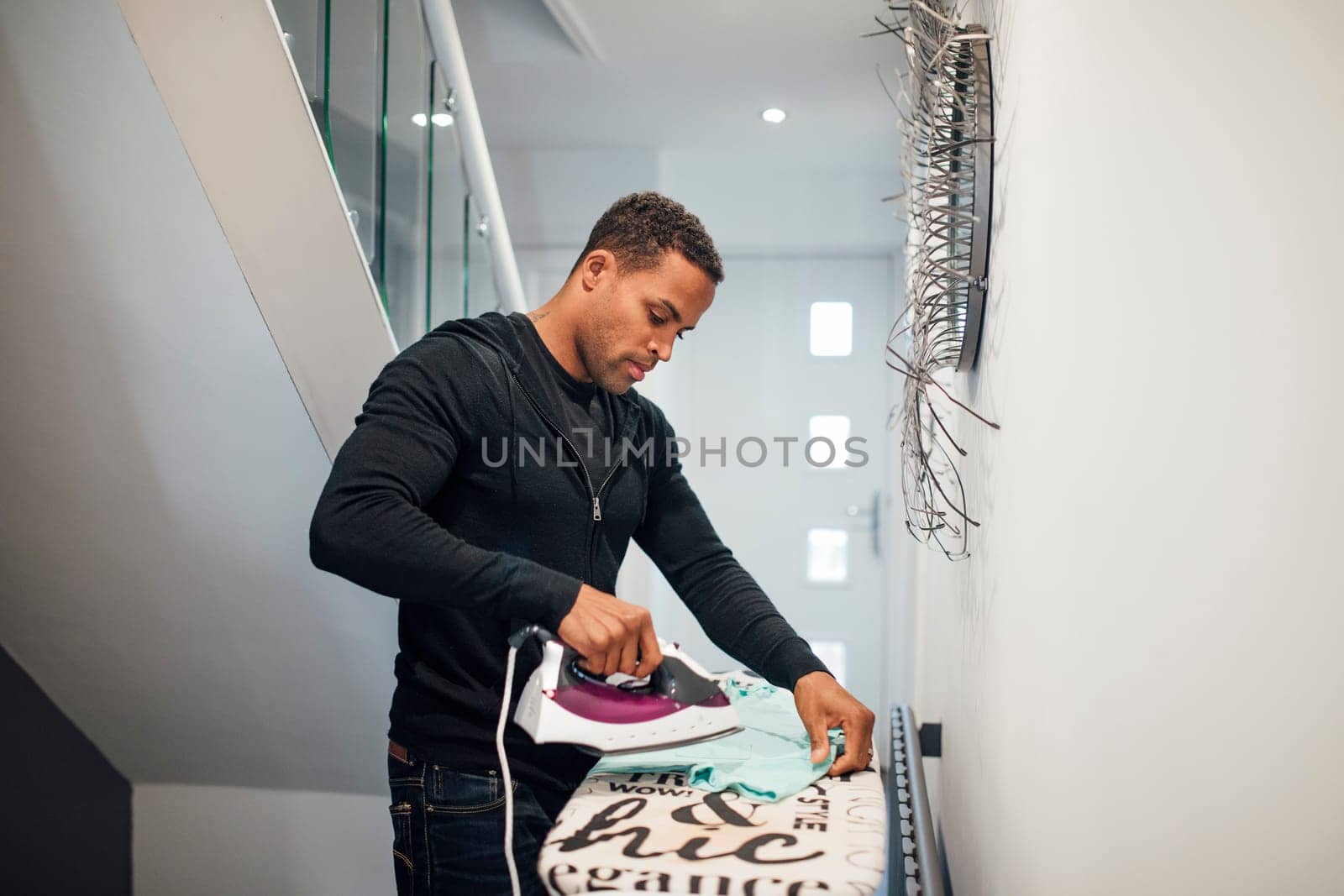 Mid adult man is ironing a school shirt in the hallway at home.