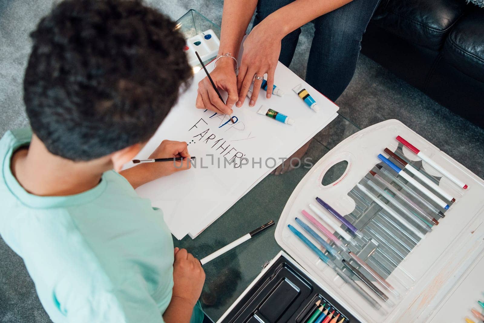 Little boy and his mother are making a Father's Day card at home using paints and crayons.