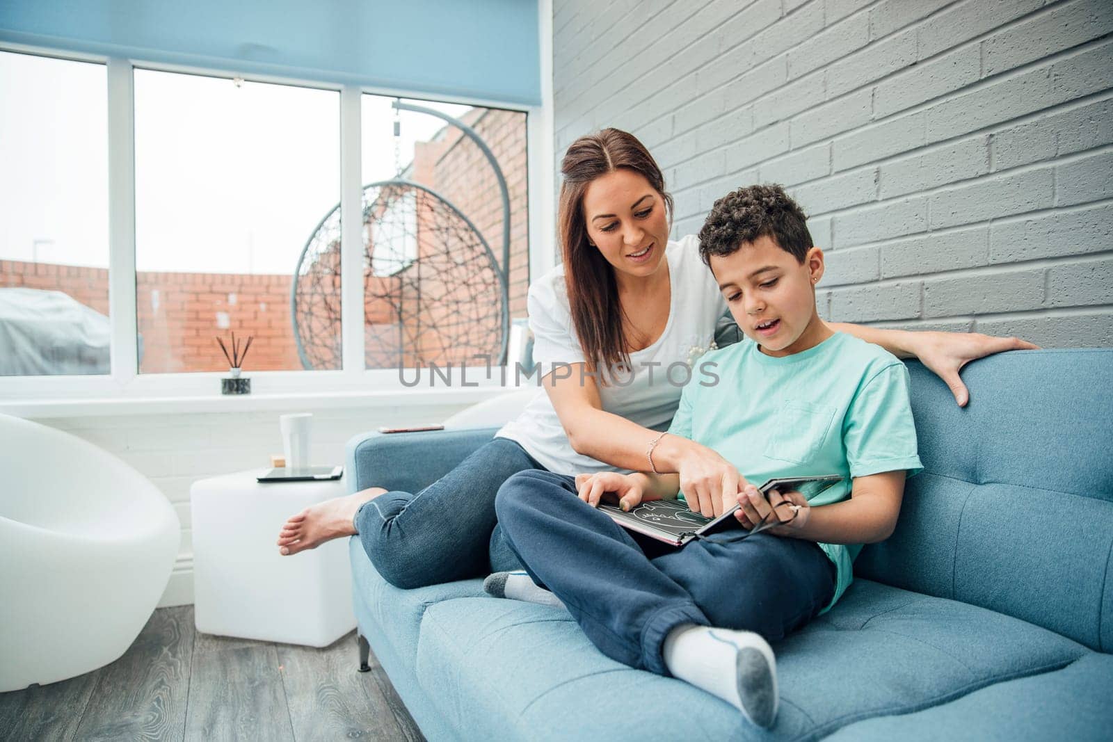 Little boy and his mother are reading a book together in the conservatory of their home.