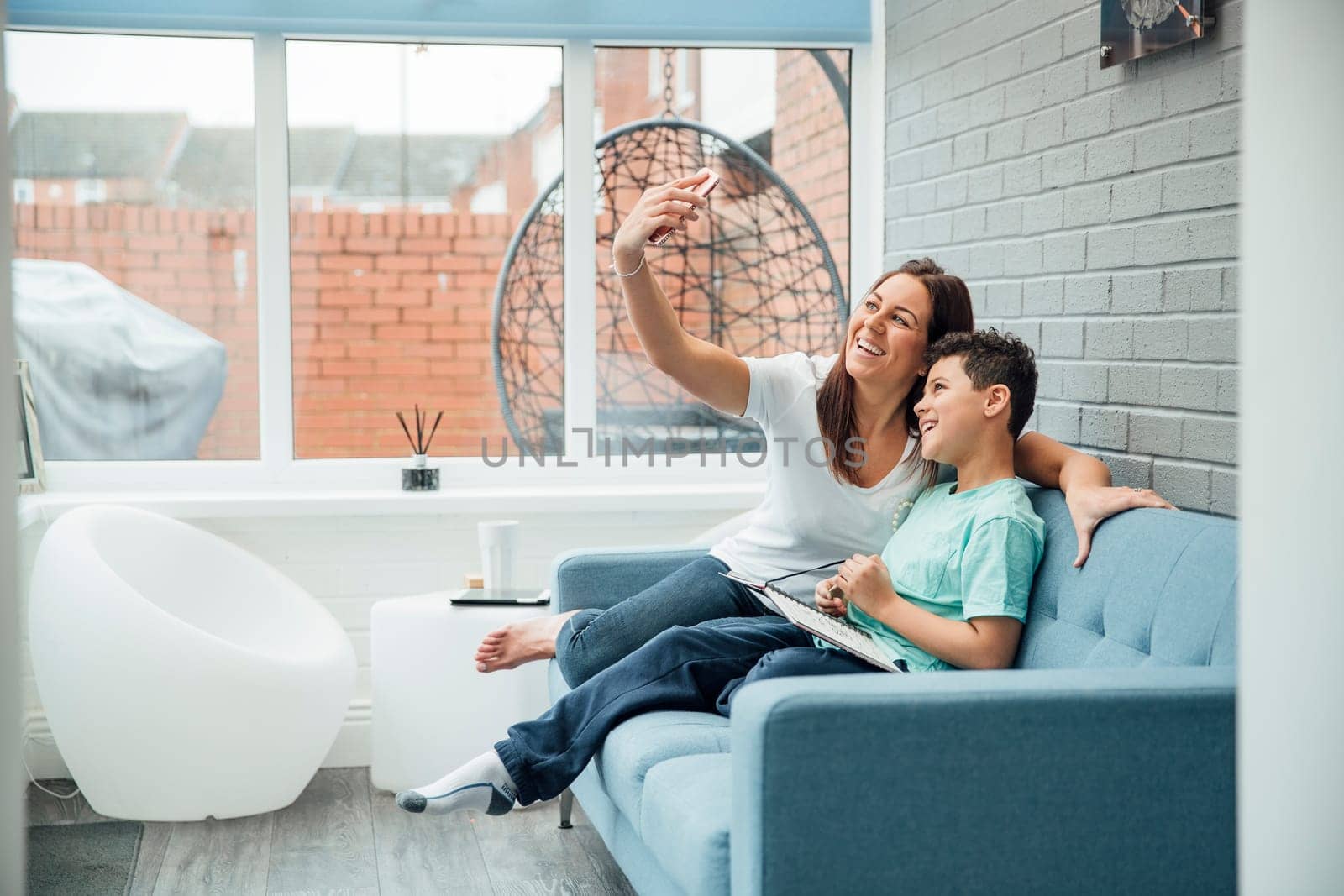 Mother and her son are taking a selfie while reading in the conservatory at home.