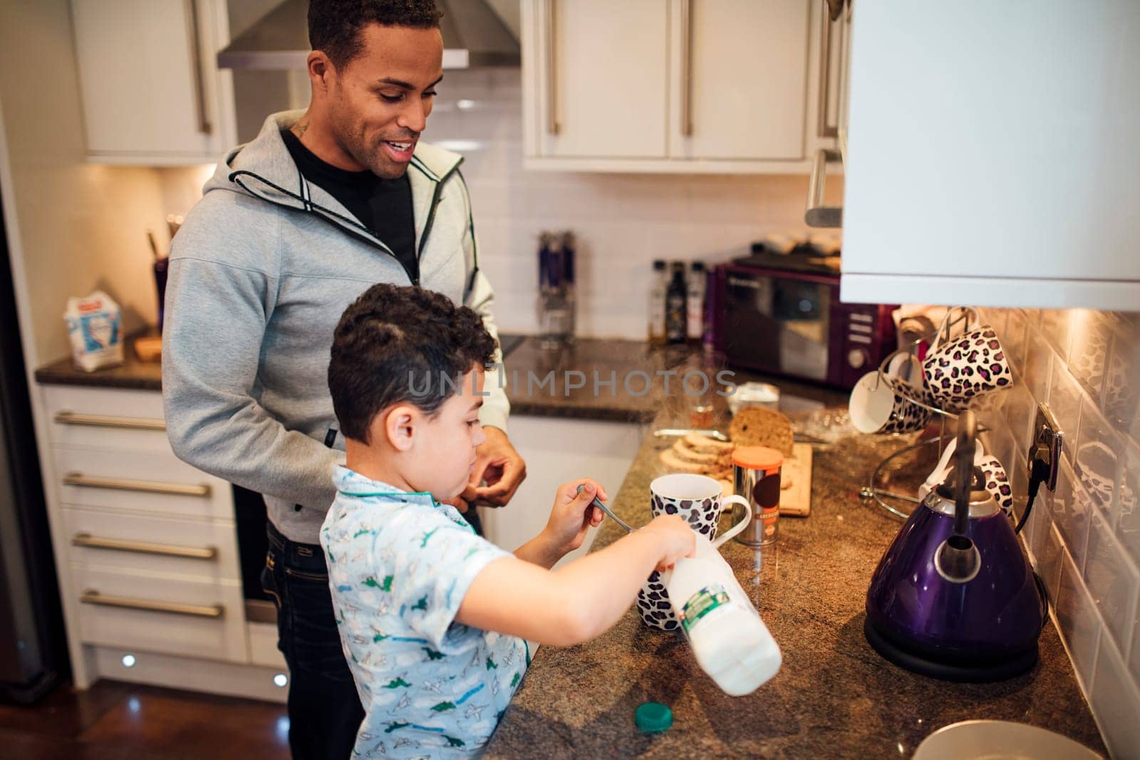 Little boy and his father are making tea for breakfast at home.