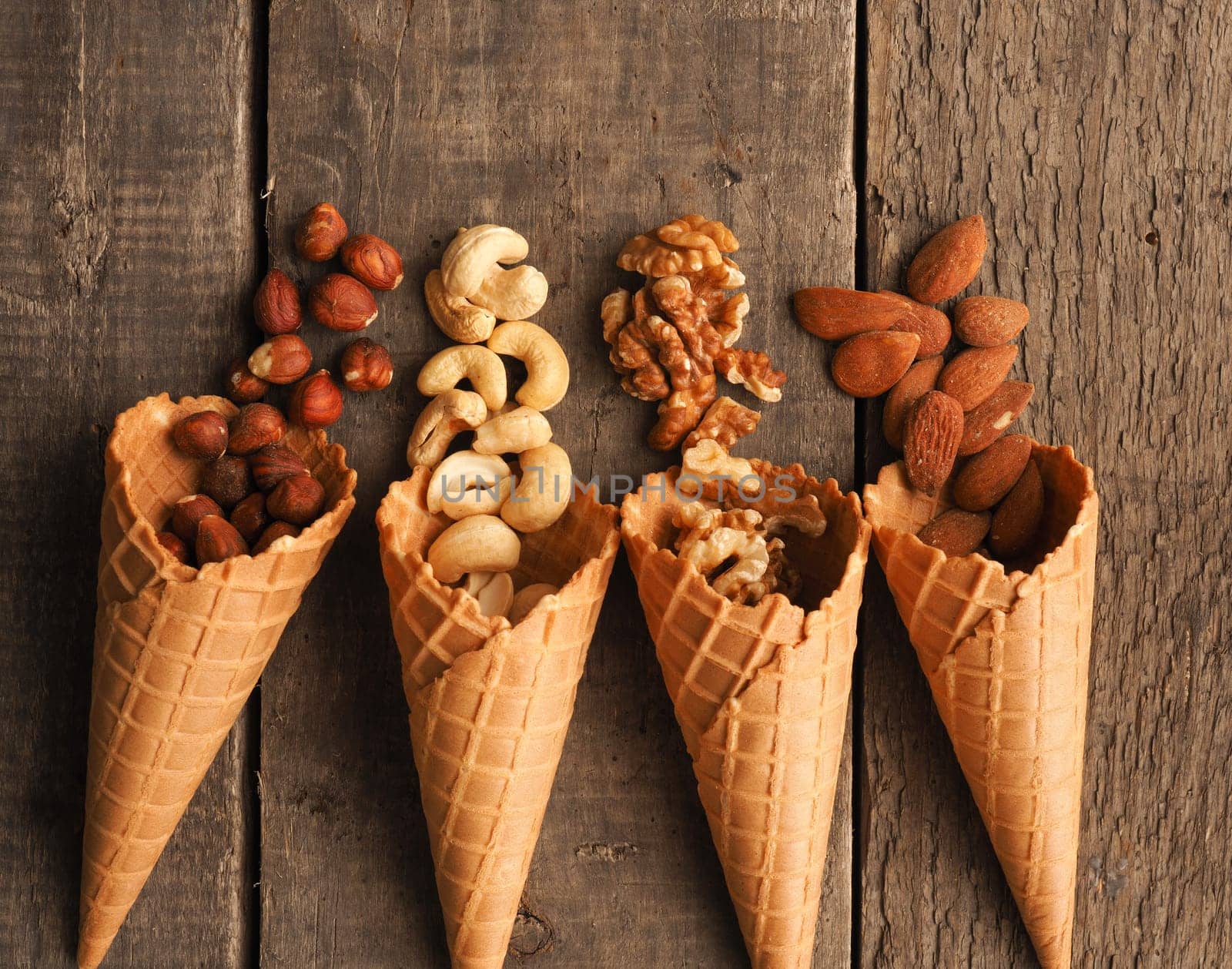 Ice cream cone with organic hazelnuts, cashews, almonds and walnuts on a rustic wooden table
