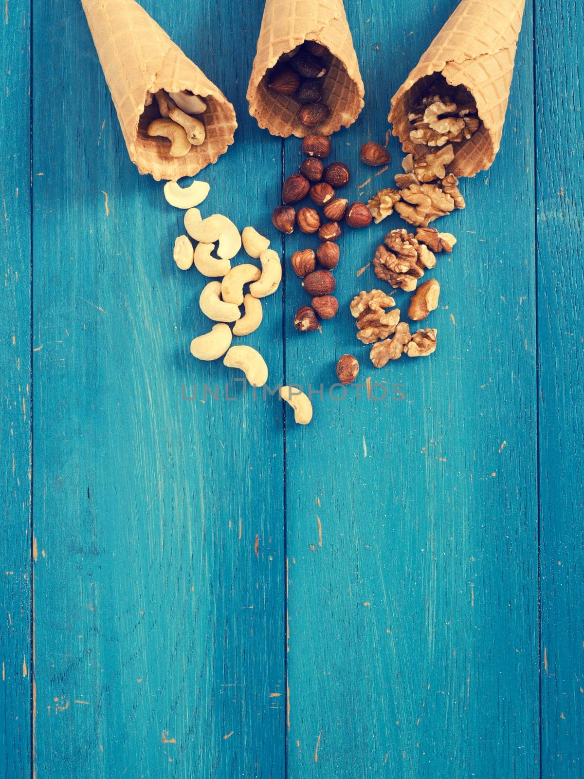Ice cream cone with organic hazelnuts, cashews and walnuts on a blue rustic wooden table
