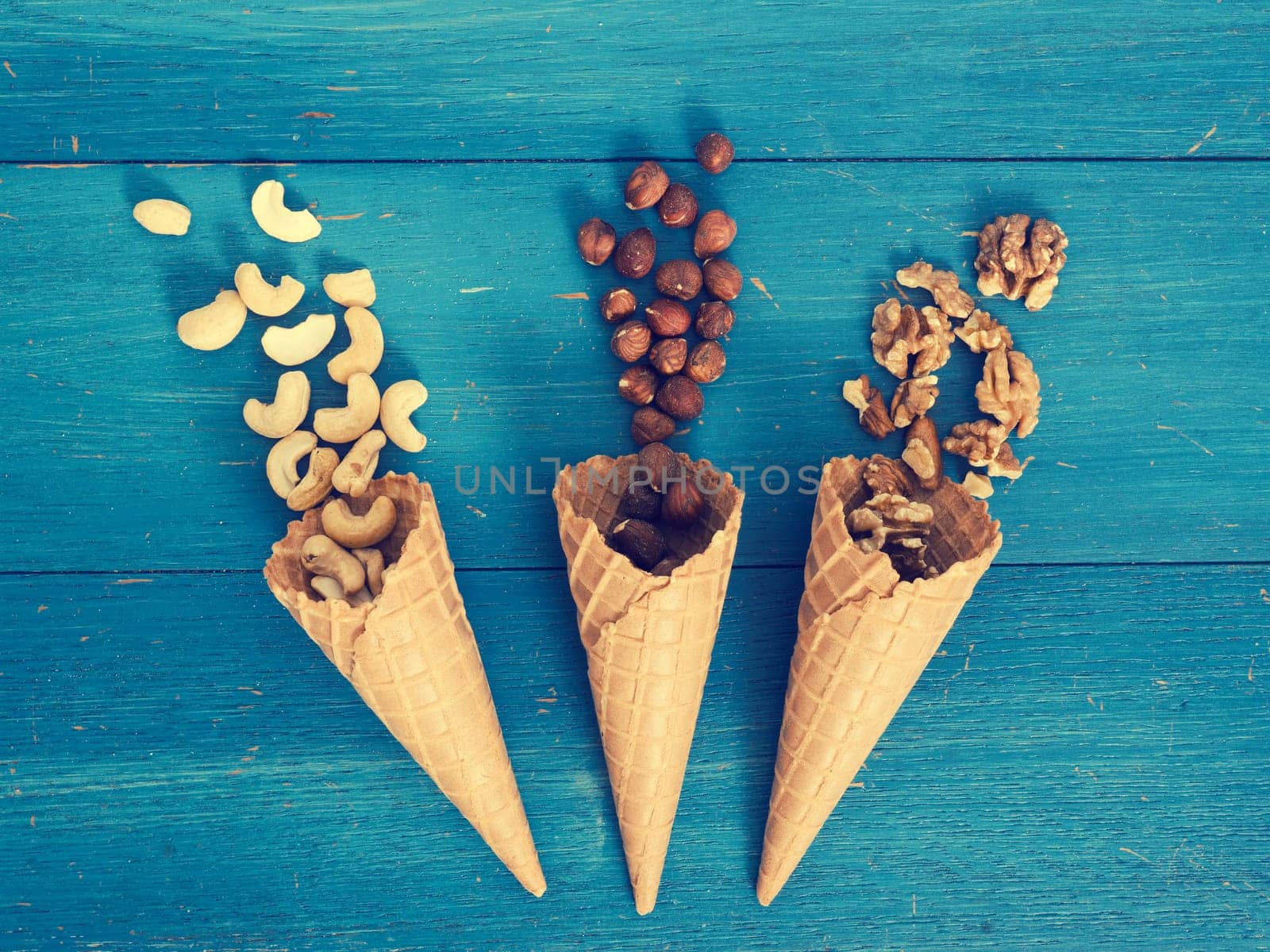 Ice cream cone with organic hazelnuts, cashews and walnuts on a blue rustic wooden table
