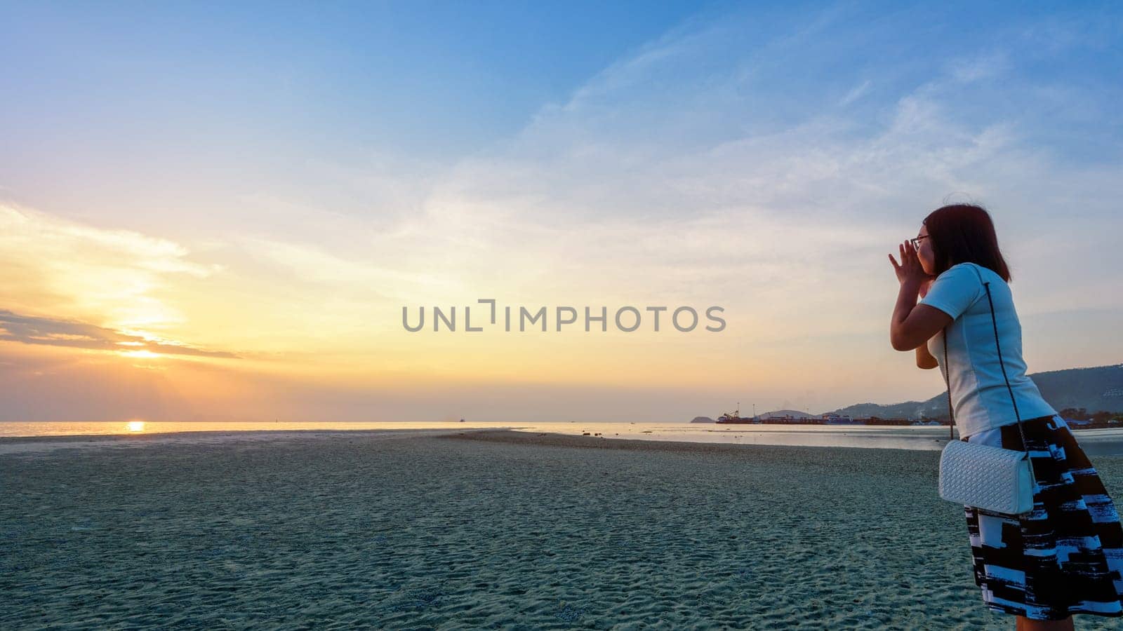 Happy women tourist raise hands at the mouth yelling and beautiful natural landscape of colorful sky and sea during a sunset at Nathon Sunset Viewpoint in Samui island, Surat Thani, Thailand, 16:9 widescreen