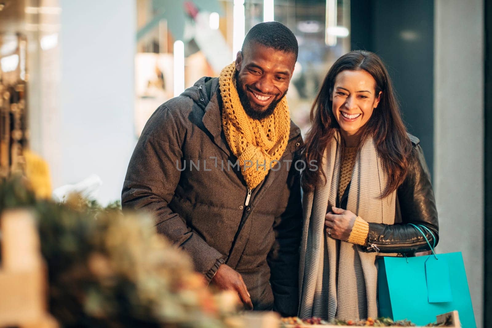 Front view of a couple standing at a christmas market stall deciding on what wreath they should buy.