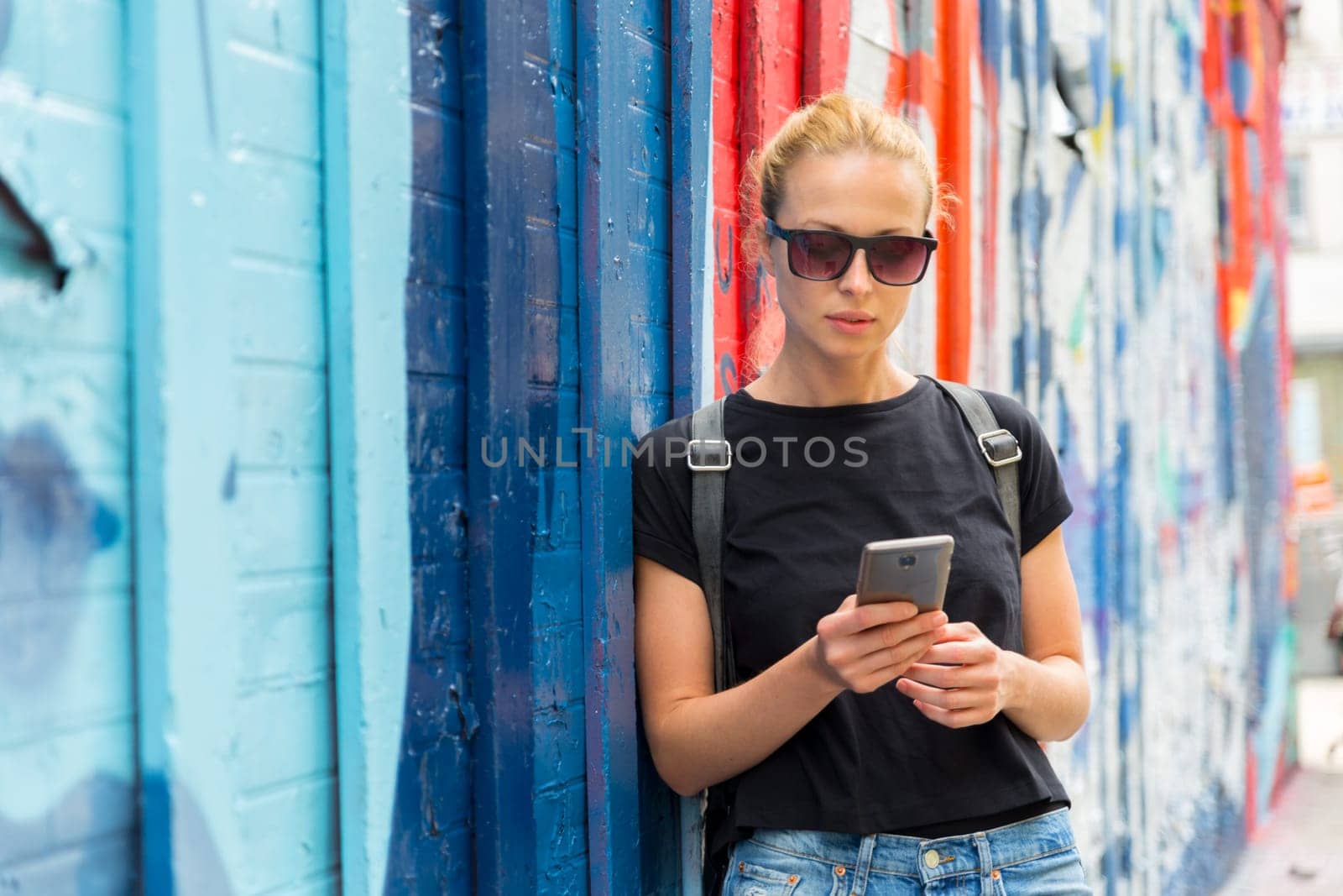 Closeup of female hipster with smart phone. Woman using smartphone against colorful graffiti wall in East Village, New York city, USA.
