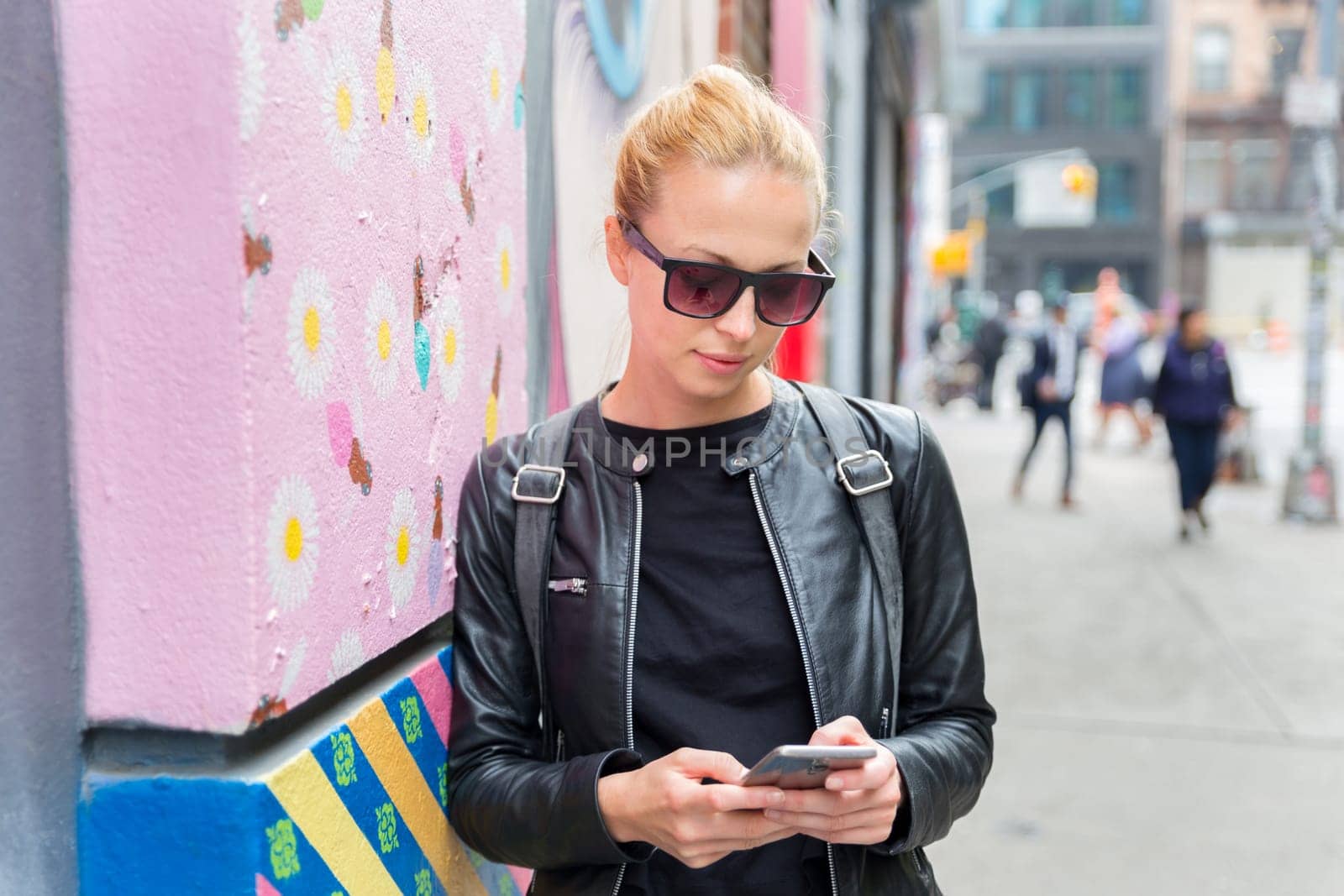 Closeup of female hipster with smart phone. Woman using smartphone against colorful graffiti wall in East Village, New York city, USA.