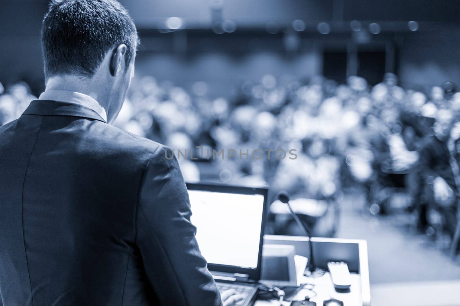 Speaker giving a talk on corporate business conference. Unrecognizable people in audience at conference hall. Business and Entrepreneurship event. Blue toned grayscale image.