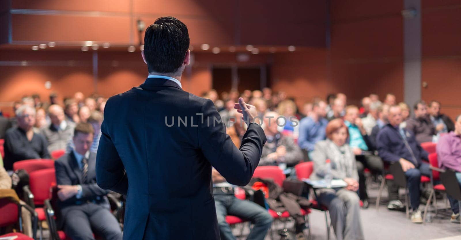 Speaker giving a talk on corporate business conference. Unrecognizable people in audience at conference hall. Business and Entrepreneurship event.