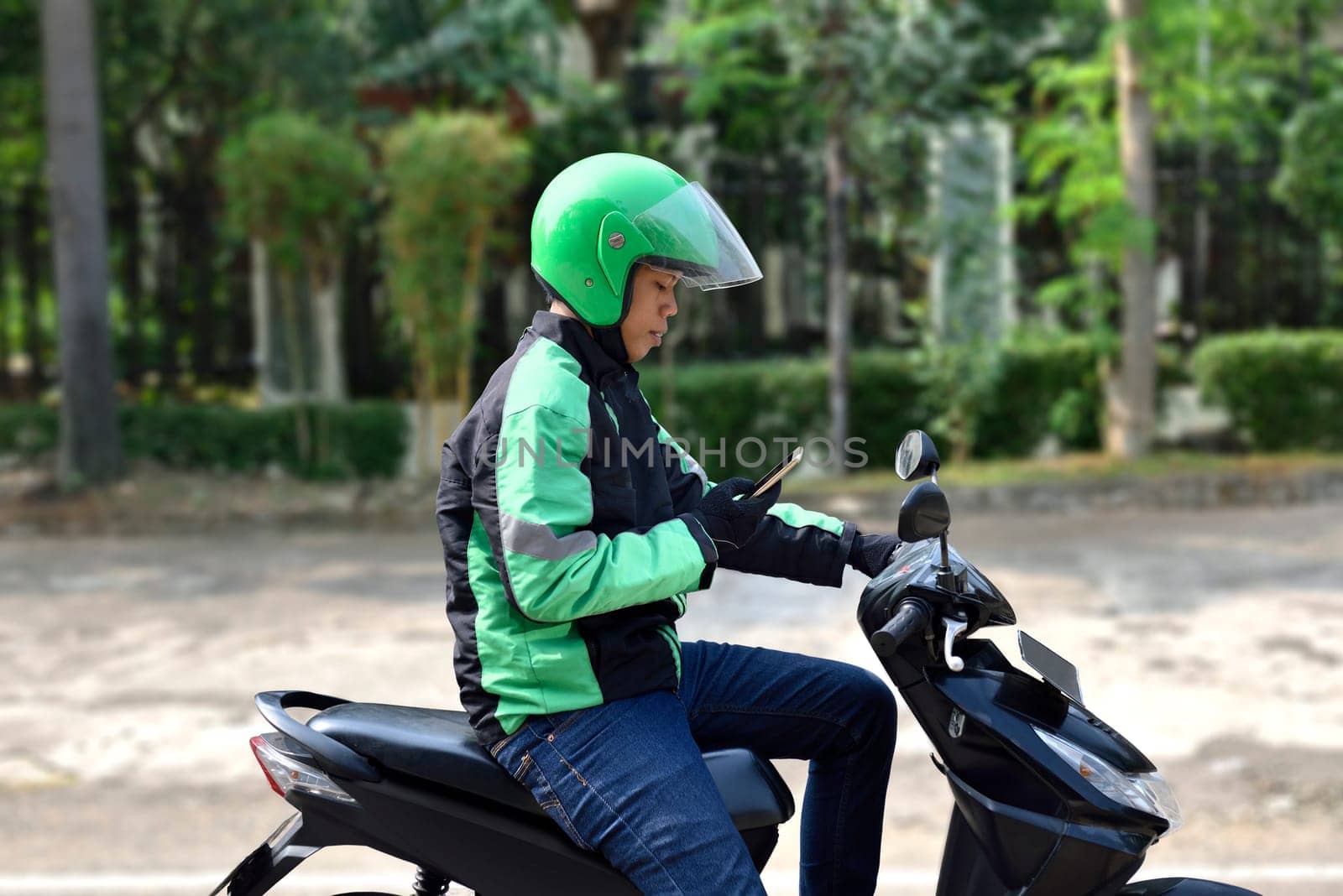 Side view of asian motorcycle taxi man checking the phone on the sidewalk