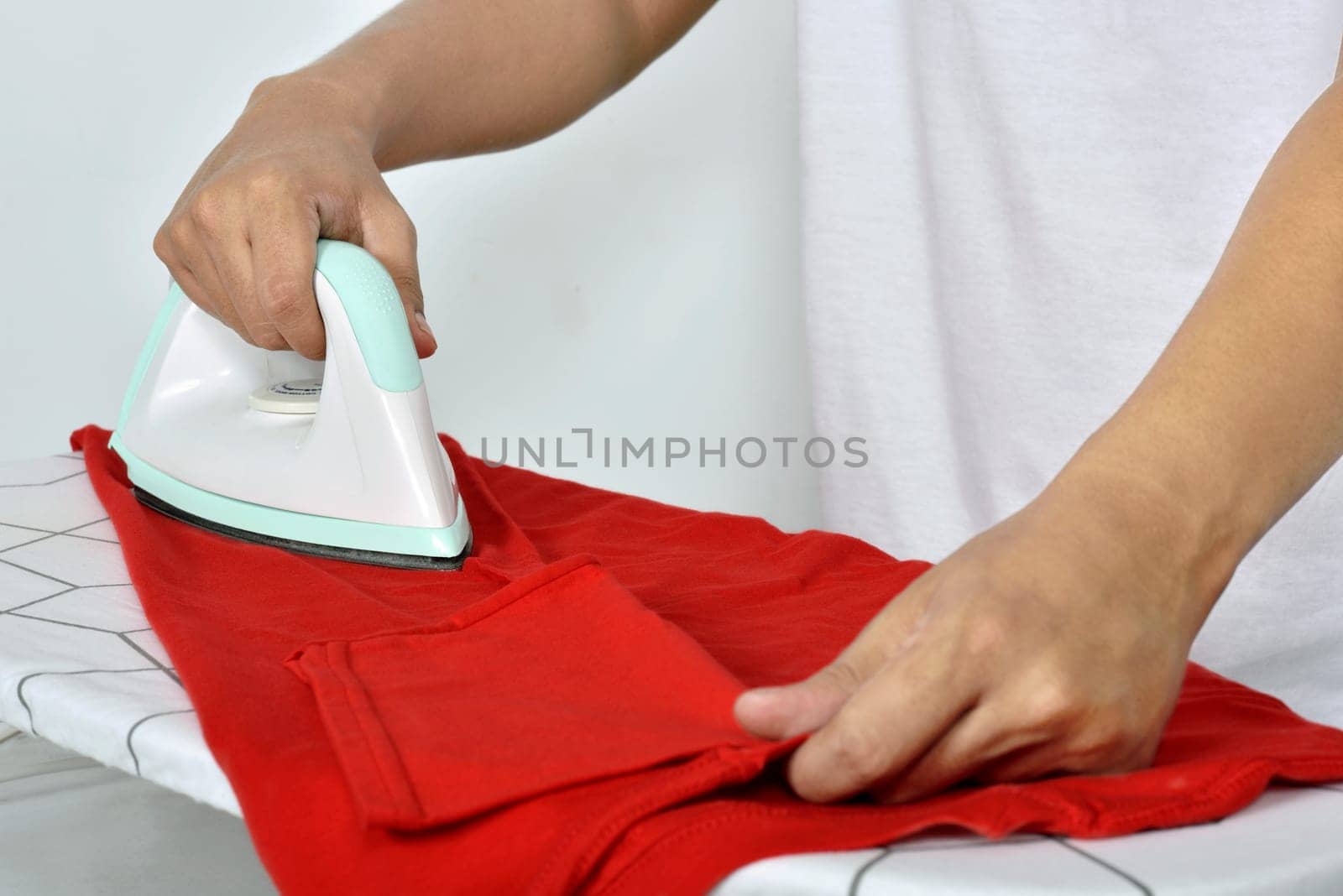 Man ironing red clothes on ironing board isolated over white background