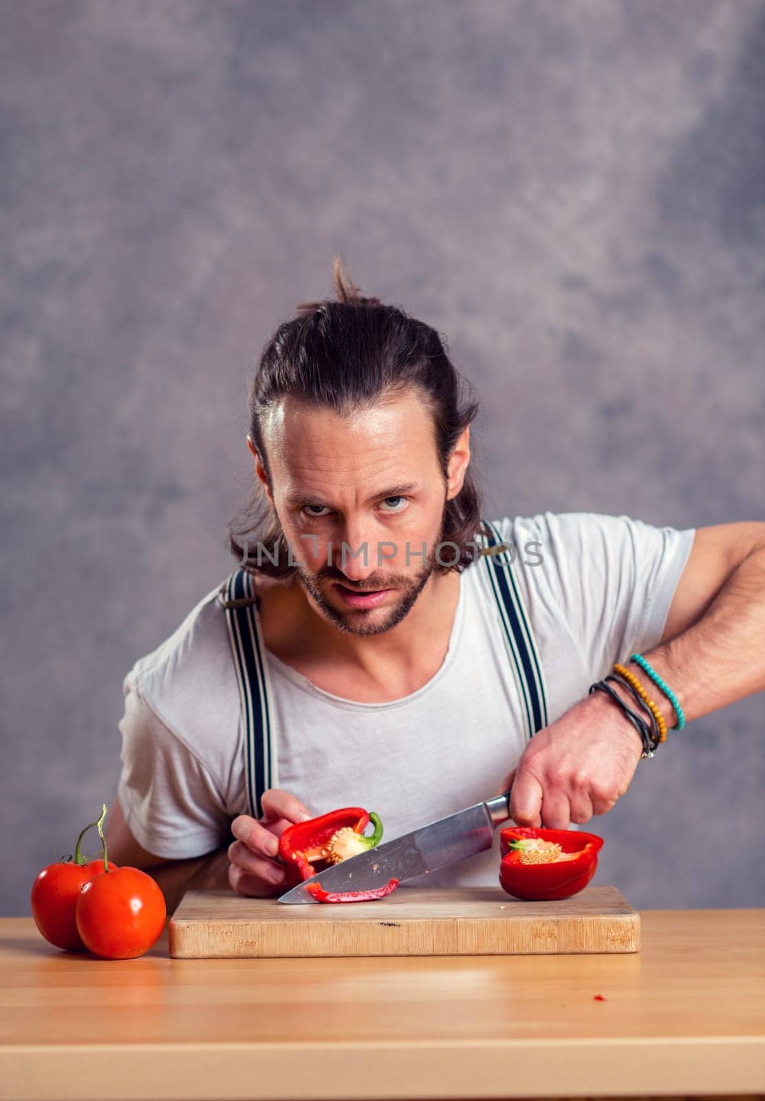 young bearded man cutting sweet pepper in front of gray background