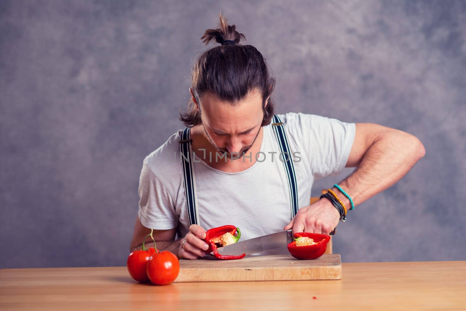 young bearded man cutting sweet pepper in front of gray background