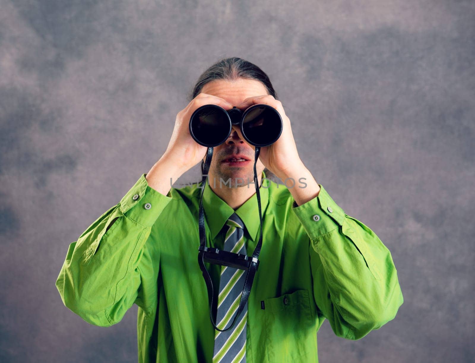 young man in green shirt and necktie looking through a binoculars