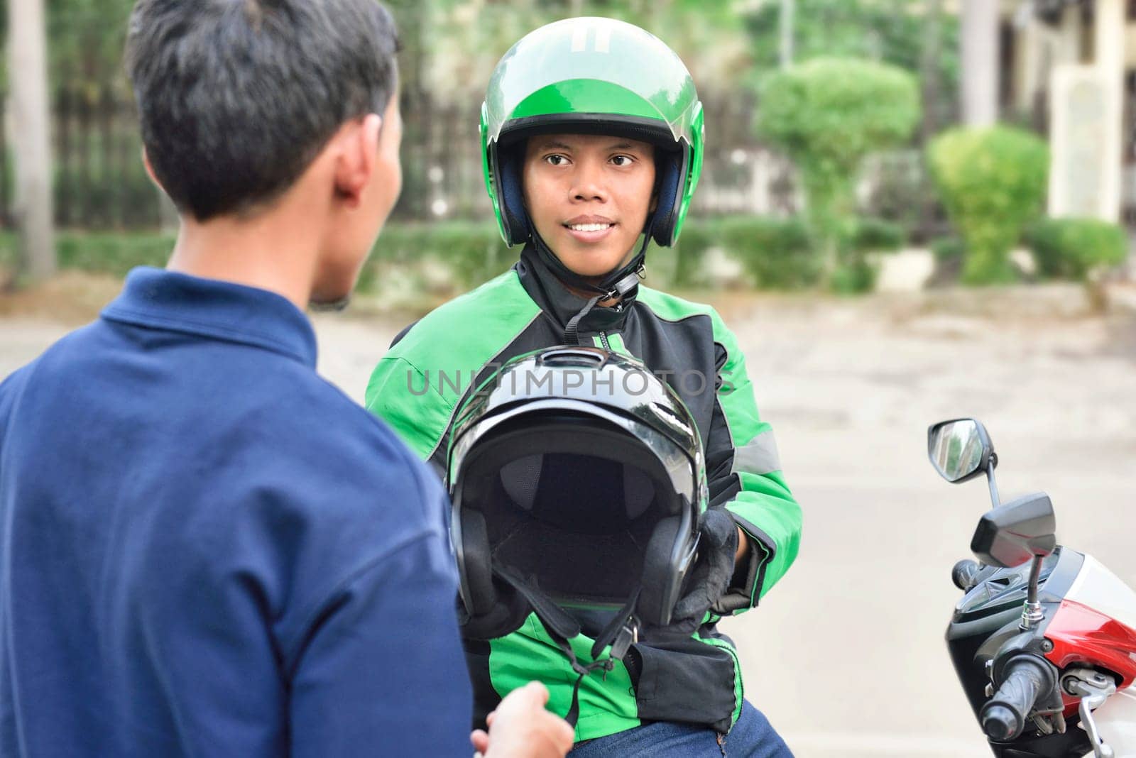 Portrait of asian motorcycle taxi driver giving the helmet to his passenger