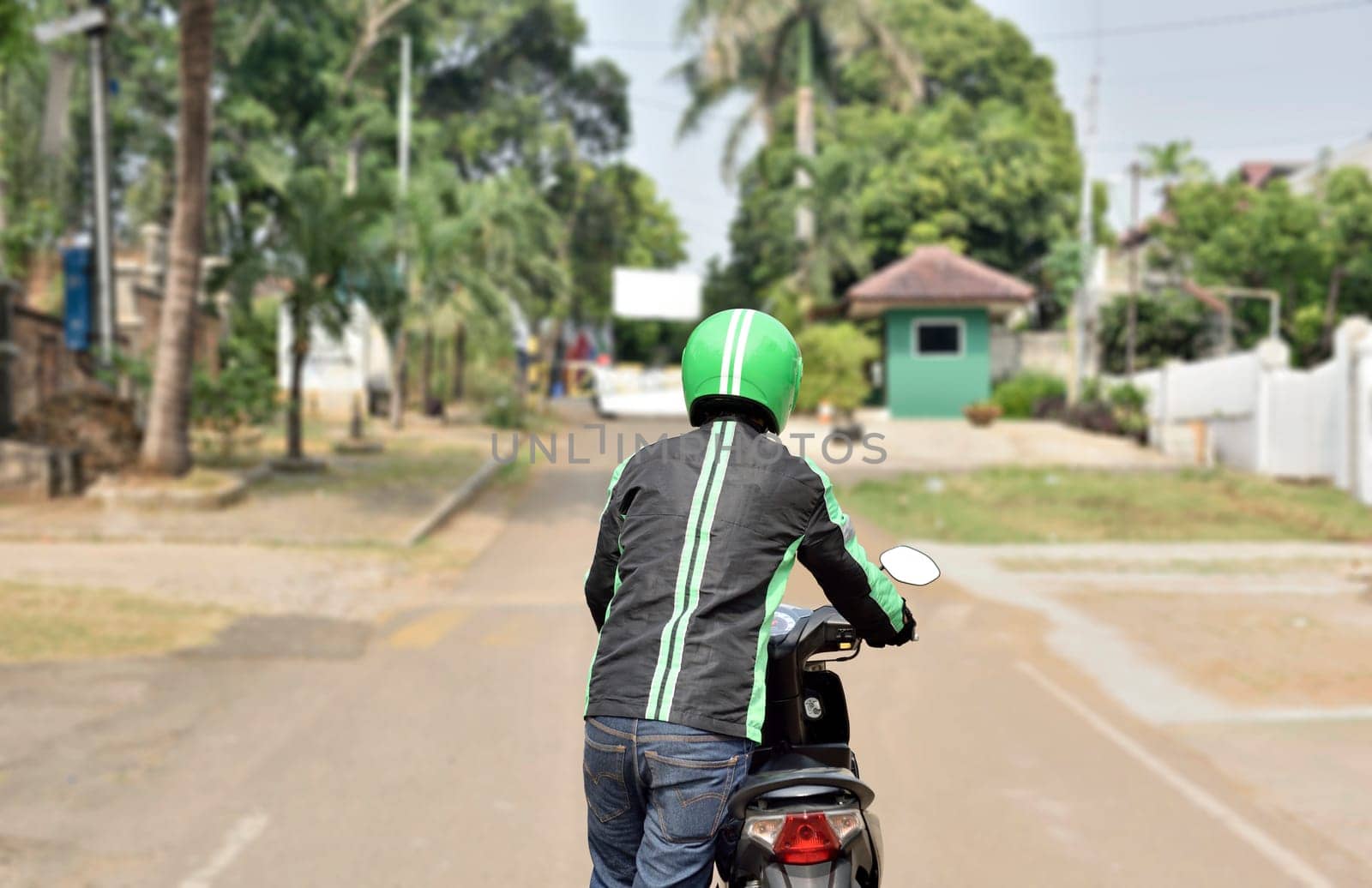 Rear view of motorcycle taxi driver pushing his motorcycle on the roadside