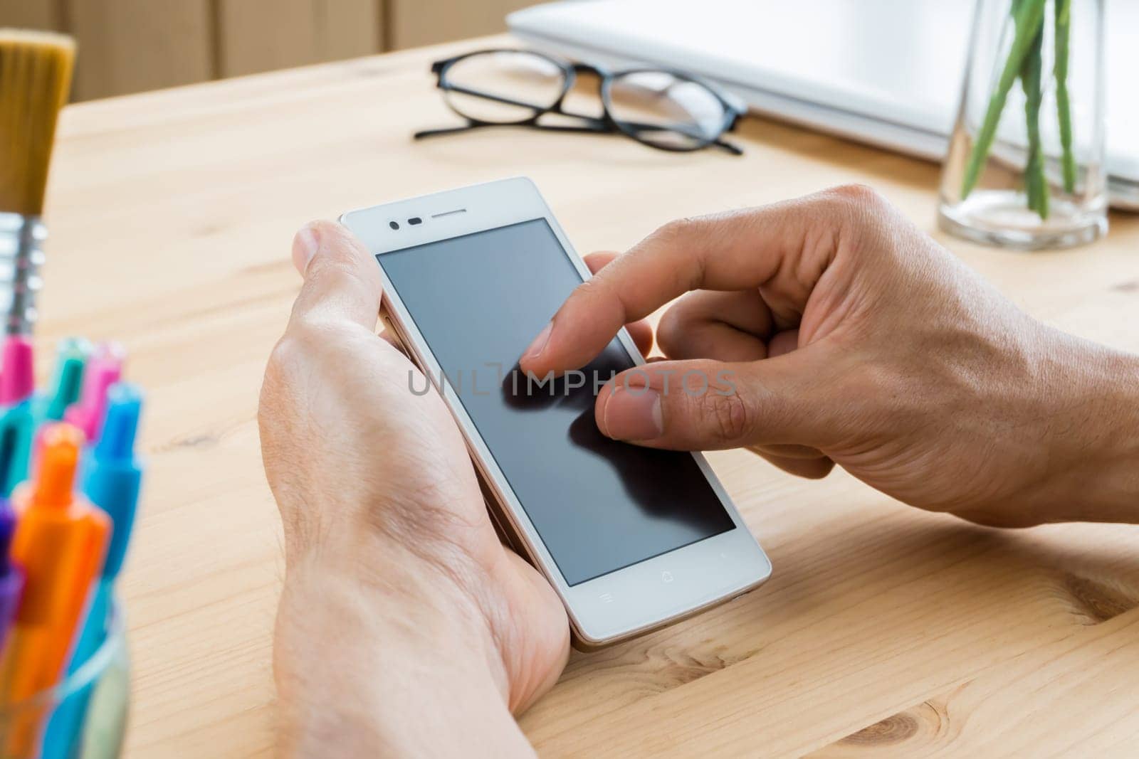 Businessman zoom in zoom out screen of horizontal smartphone or mobile phone in close up. Smartphone or mobile phone and pen and .eyeglasses and laptop or notebook on wood table in home office