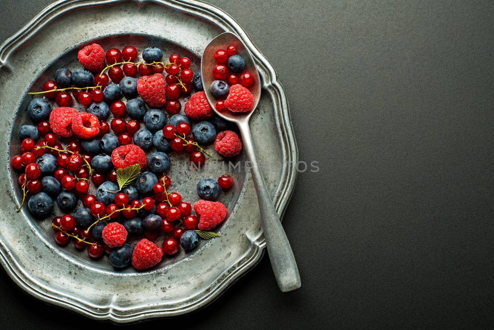 Mix of fresh berries in a plate on black background