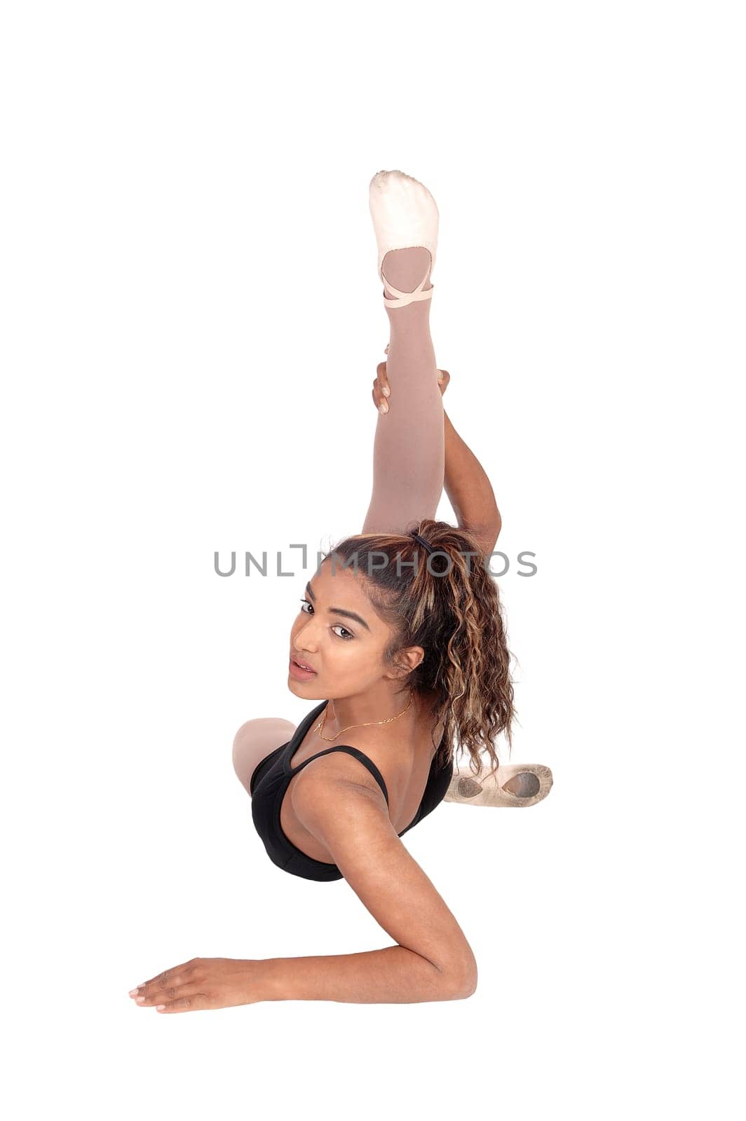 A slim young woman in an ballet outfit sitting on the floor with one.leg up doing warm up exercises, isolated for white background.