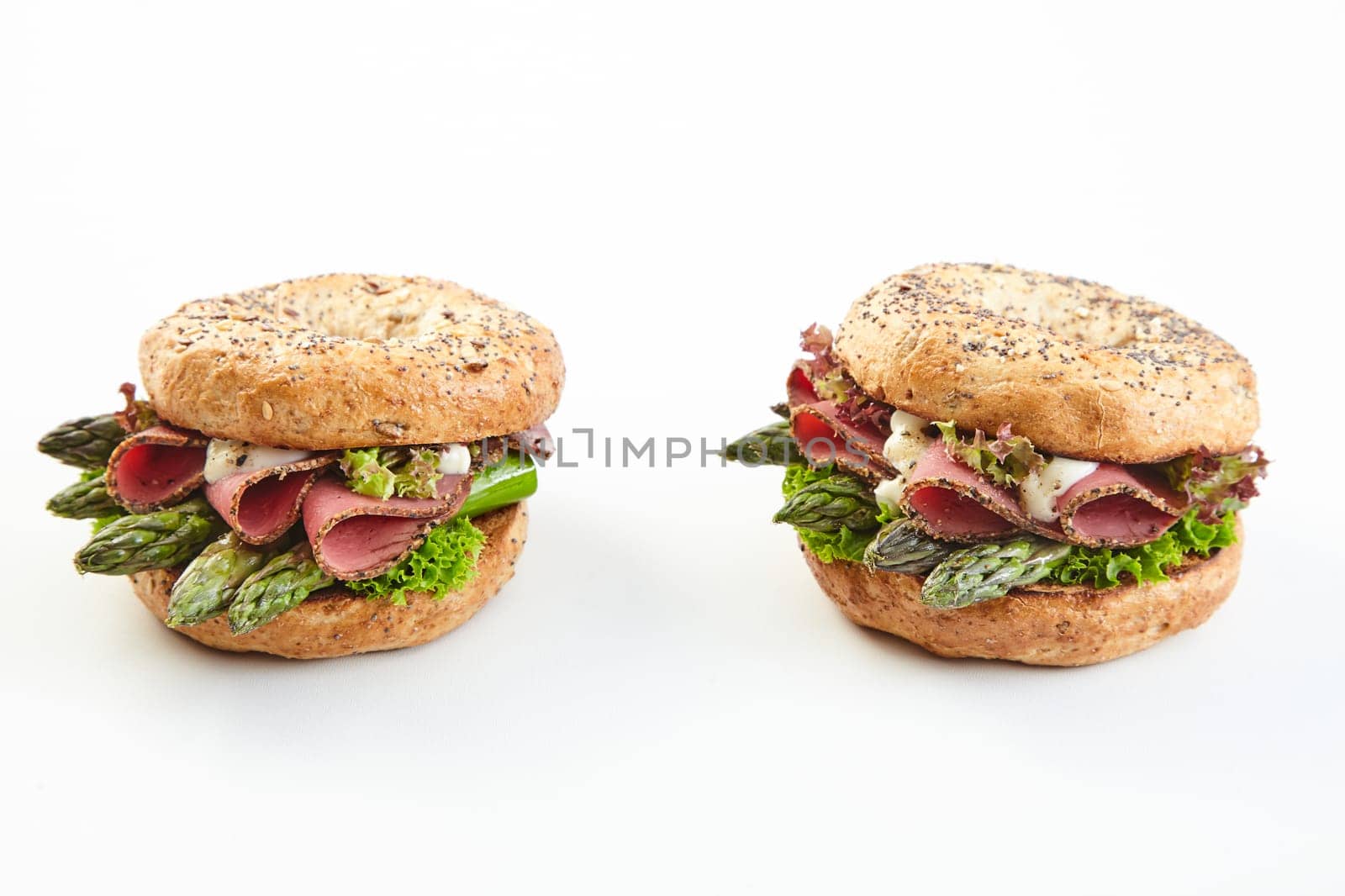 Two gourmet seasonal spring asparagus burgers with fresh green spears topped with ham and mayonnaise on two buns over white with copy space