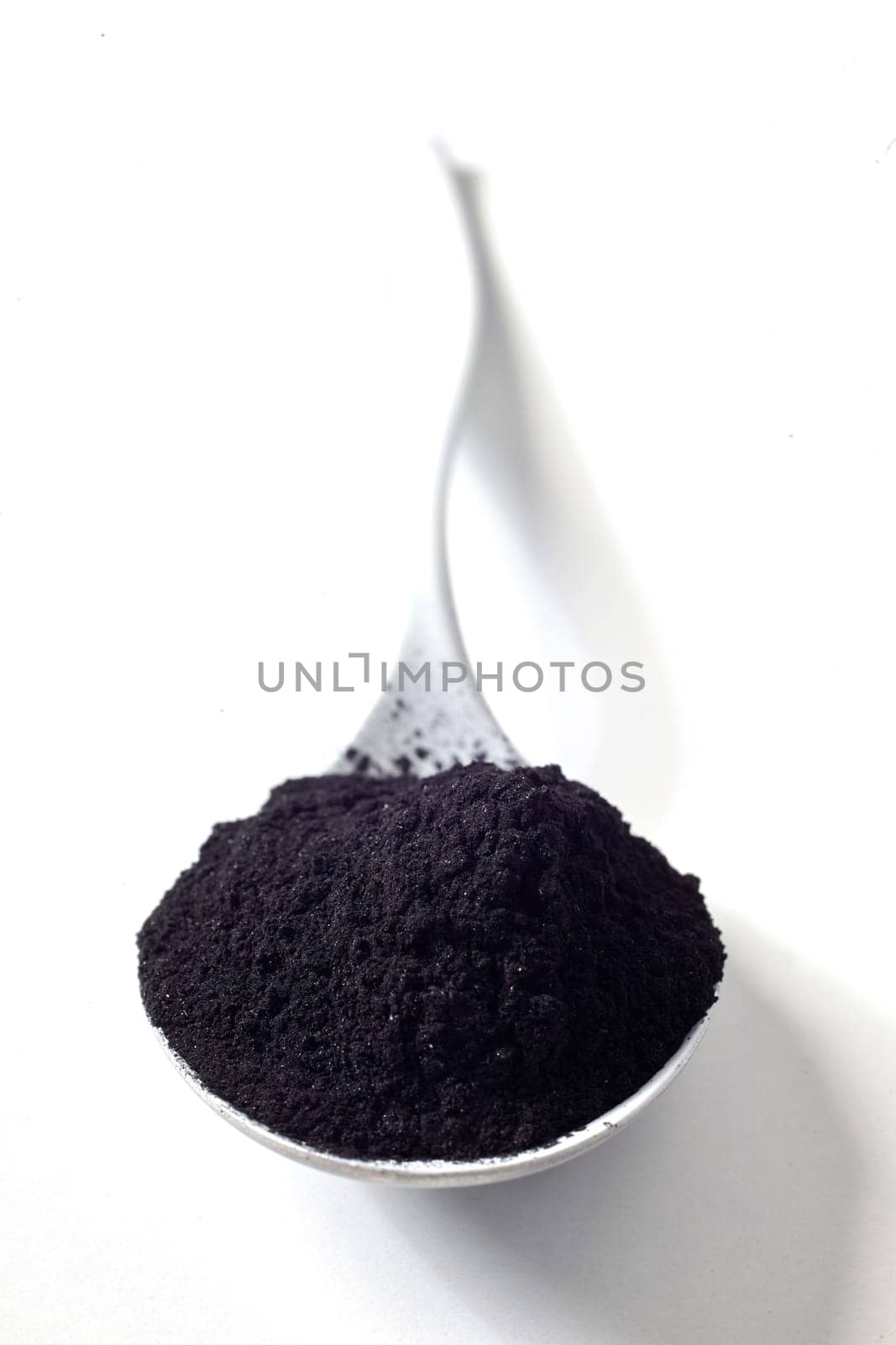 Heap of organic food grade charcoal in a spoon over white used as a heath additive for cleansing and detoxifying