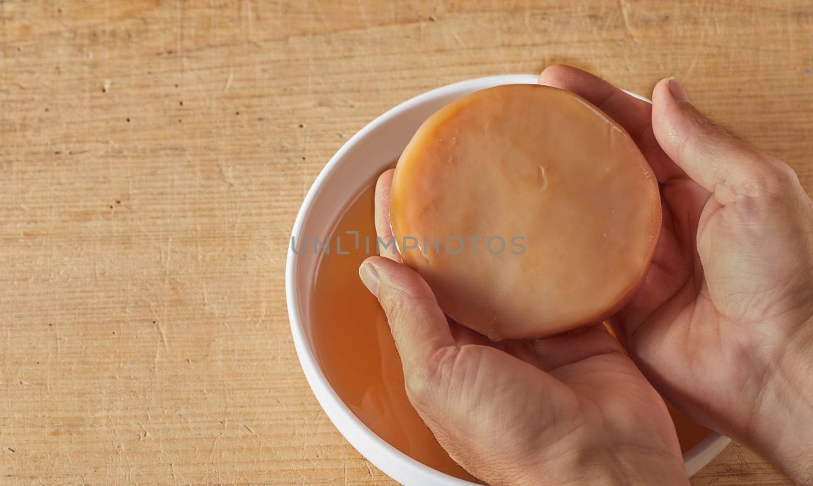 Hands holding kombucha scoby tea mushroom against wooden table