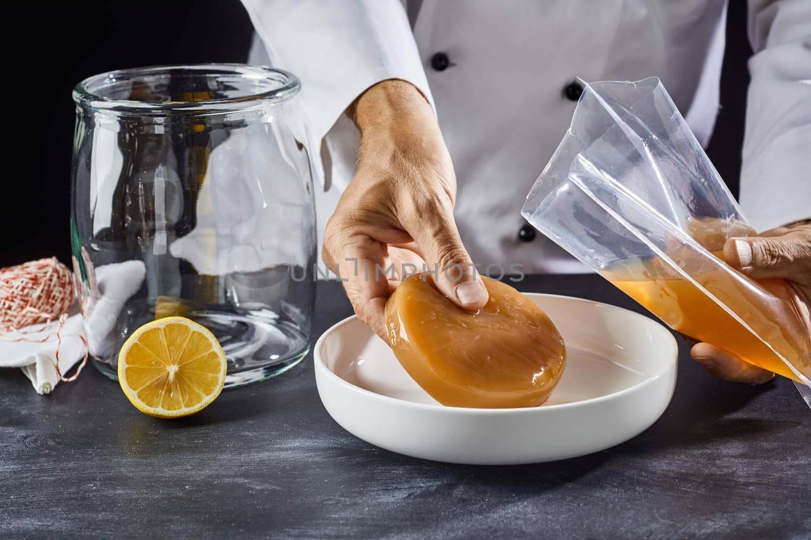 Man placing a scoby, fungus, mother, zoogleal mat or mushroom in a dish for activation while preparing homemade kombucha