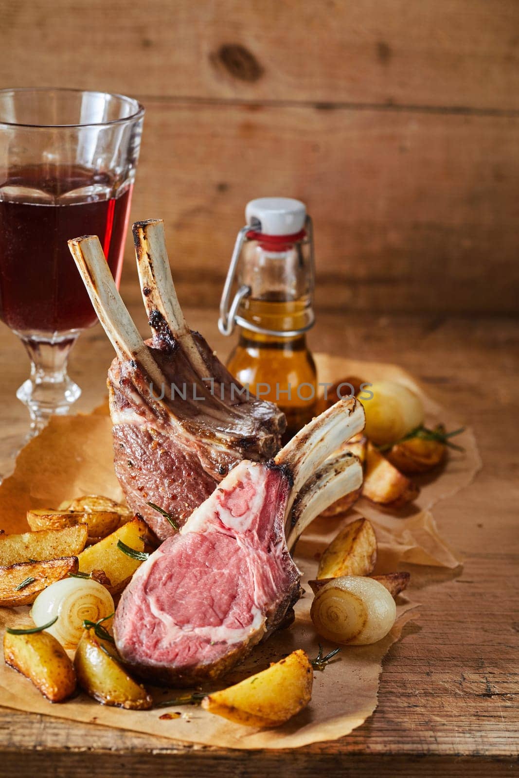 Serving of spicy seasoned barbecued lamb chops with roasted potatoes and onions in a rustic tavern served with a glass of red wine and beer