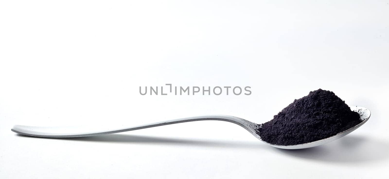 Silver spoon heaped with pulverised organic charcoal used as a food and drink additive for cleansing and detoxifying the body over white with copy space
