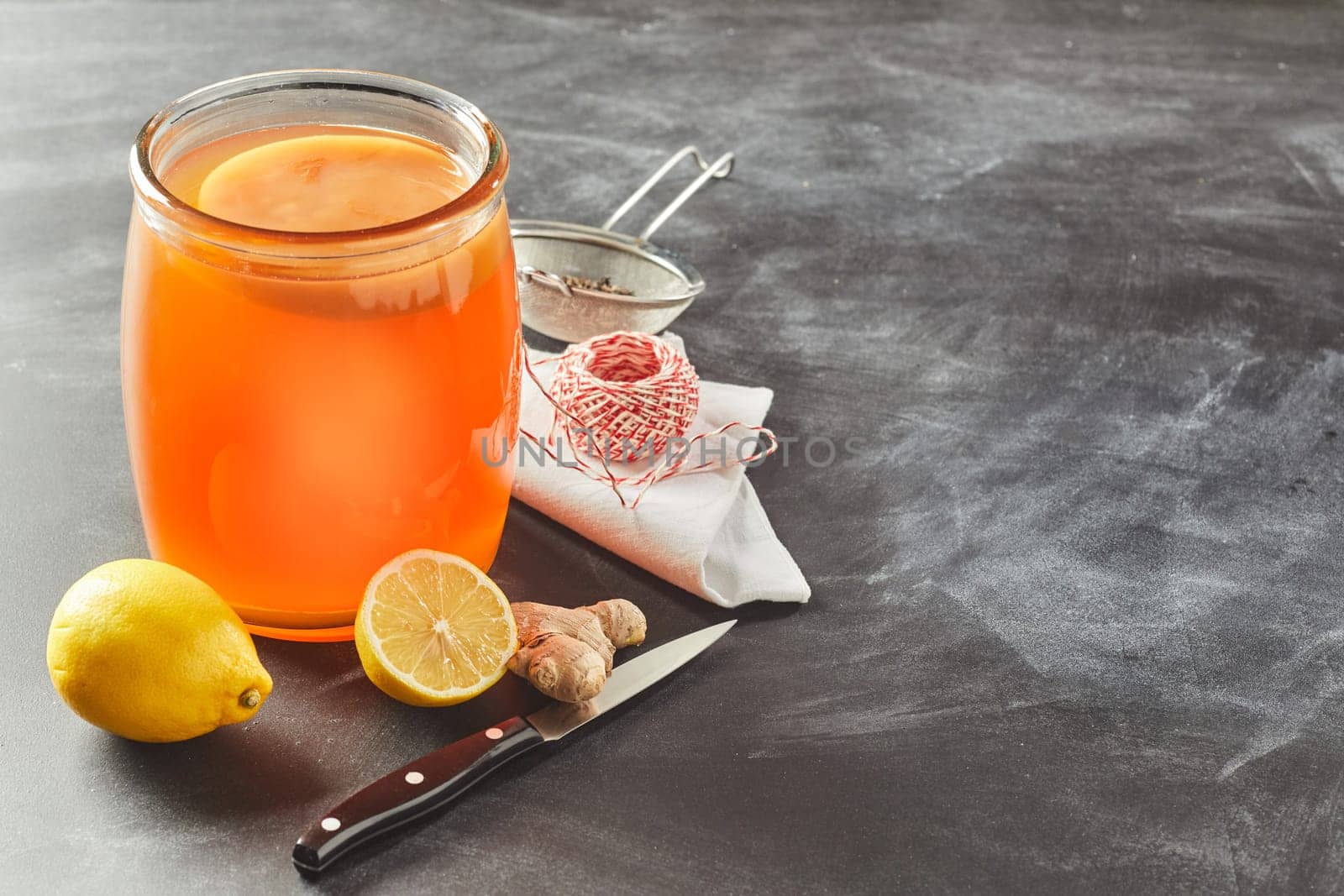 Fermented glass jar of black tea kombucha with fresh lemon and root ginger on a slate background with copy space