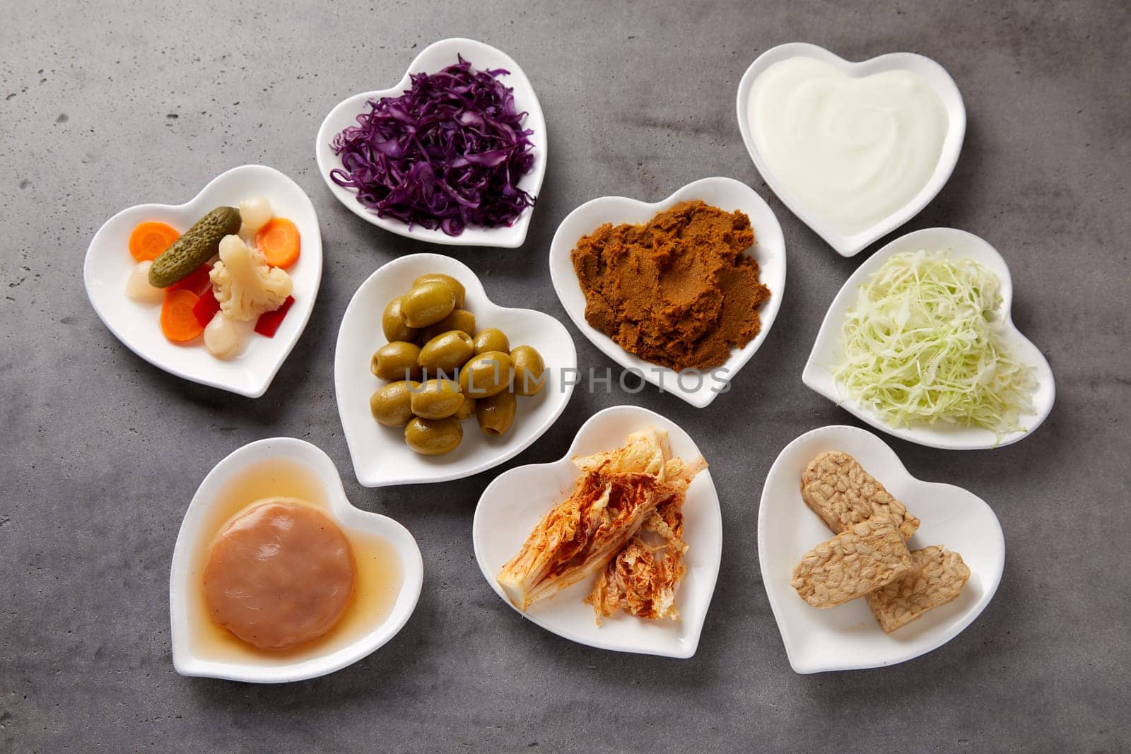 Assorted fermented foods viewed from above in heart-shaped dishes with yogurt, beet, suaerkraut, scoby, pickles, miso and olives rich in probiotics and microorganisms essential for a healthy gut