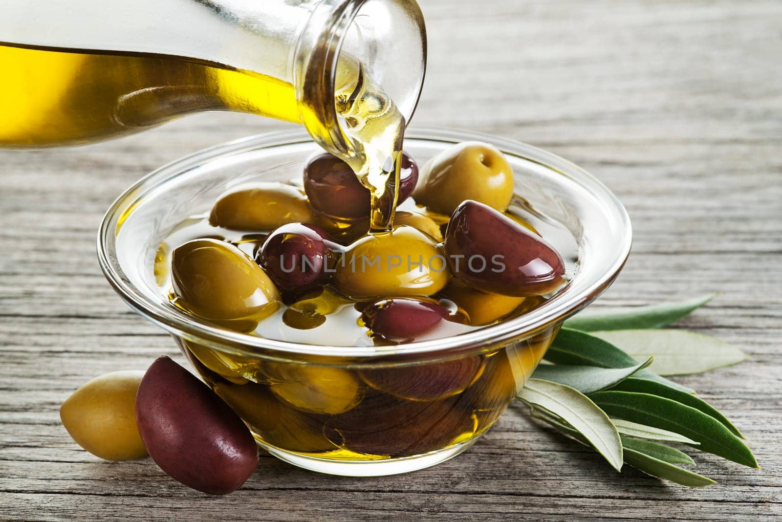 Bottle pouring virgin olive oil in a bowl with olives close up