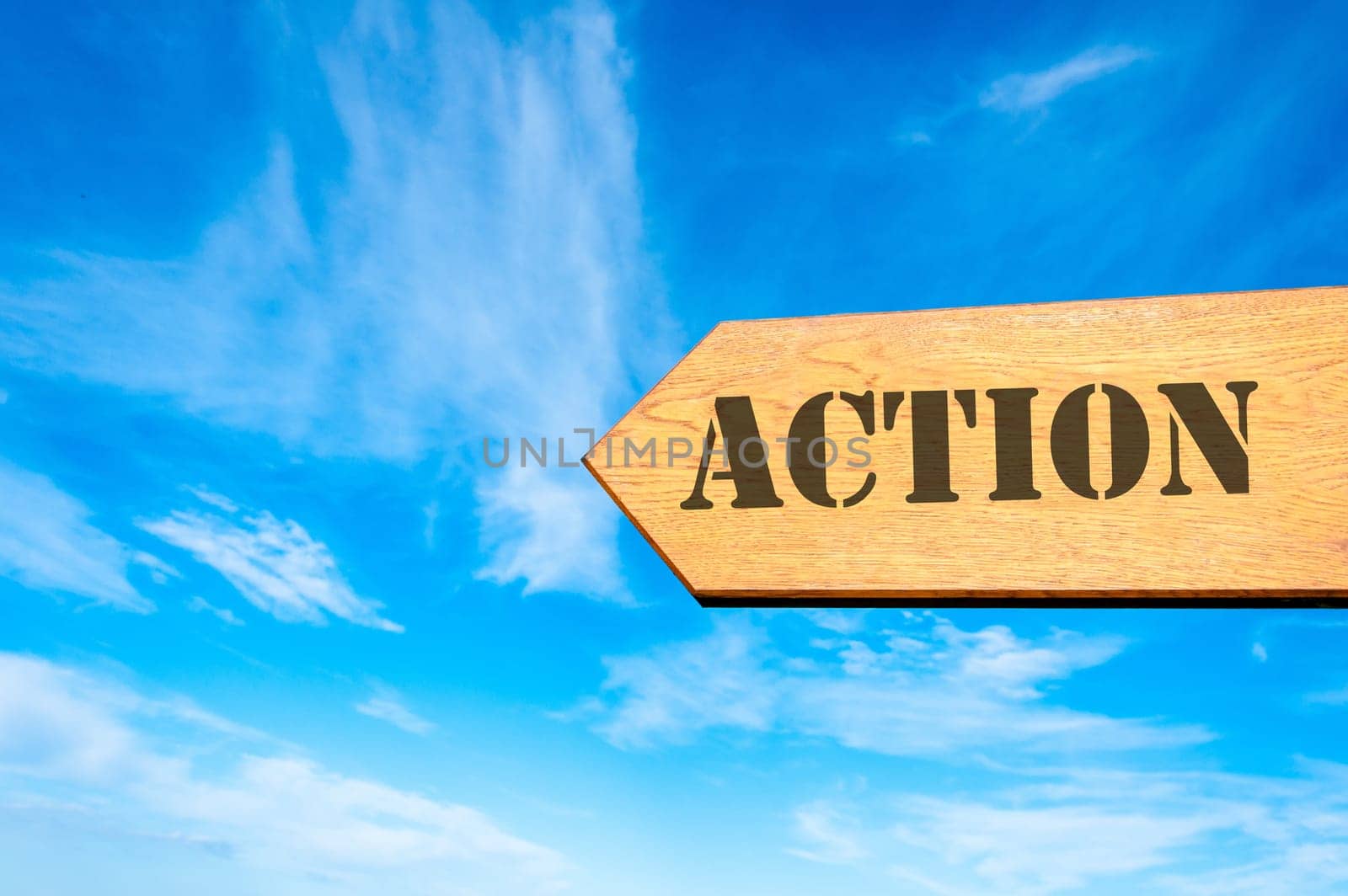 Wood arrow sign against clear blue sky with Action message