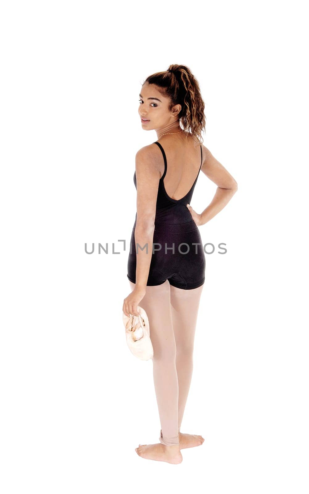 A young beautiful tall woman standing in a black ballet outfit from the.back with her ballet shoos in her hand, isolated for white background.