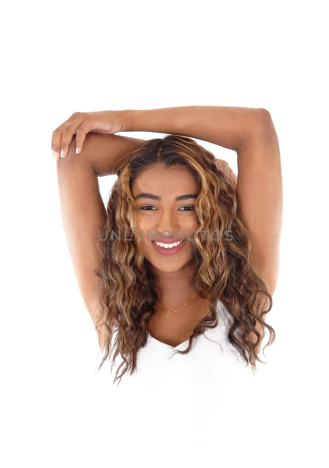 A gorgeous young woman with curly brunette hair standing in closeup.with her arms over her head and smiling, isolated for white background.