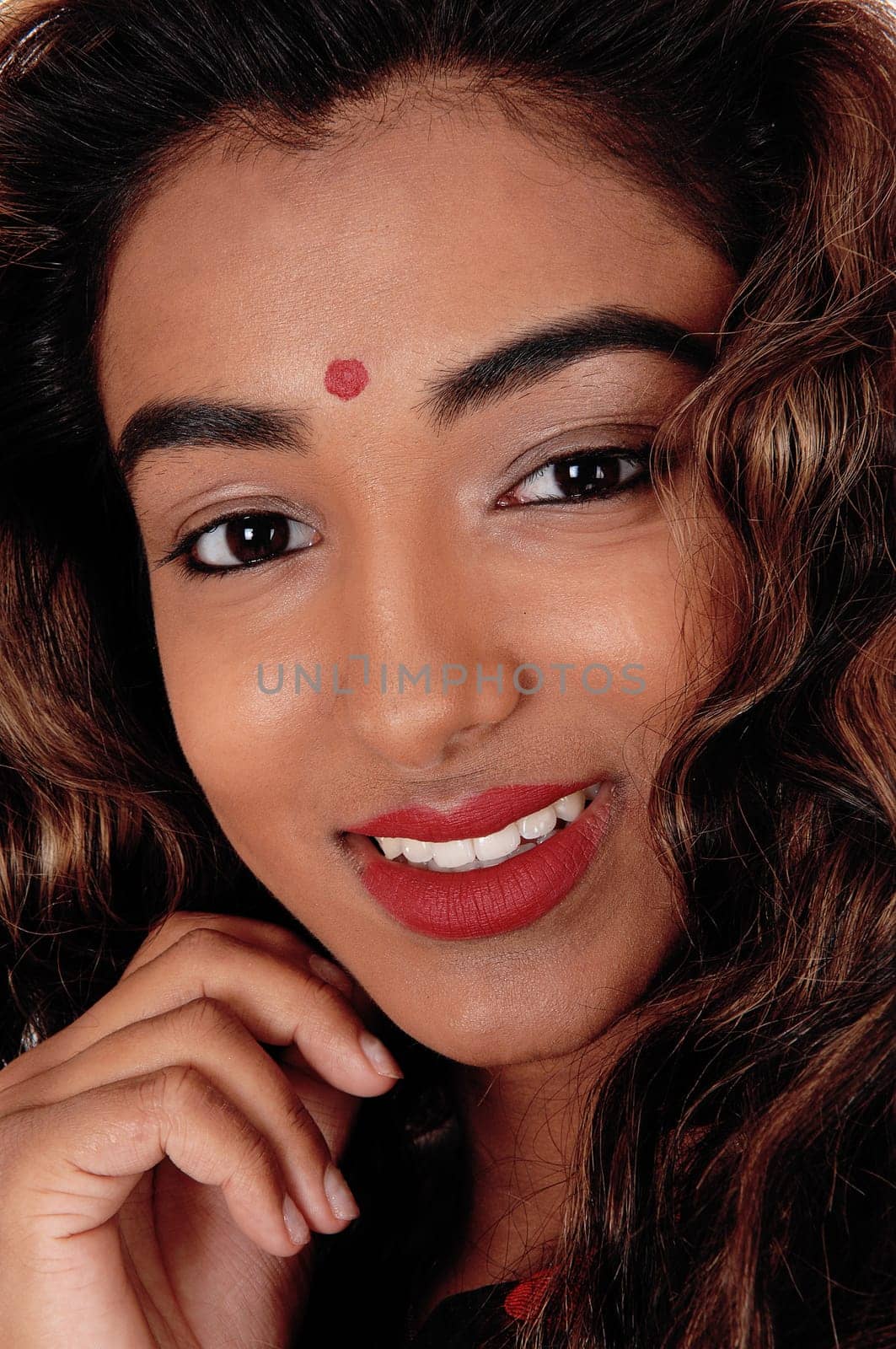 A close up image of the face of a gorgeous young teenager girl with curly.brunette hair with one hand on the face, isolated .