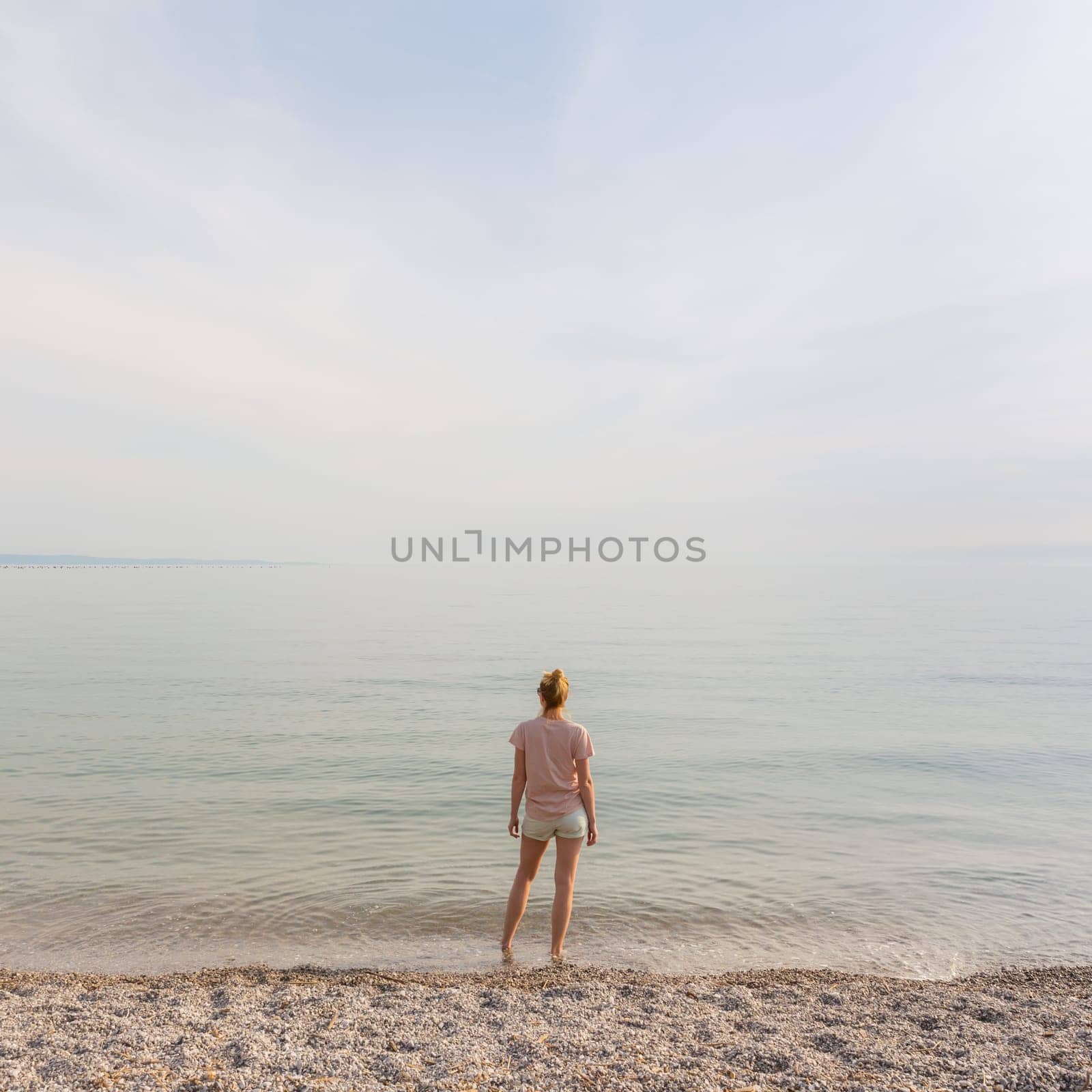 Happy Carefree Woman Enjoying Late Afternoon Walk on White Pabbled Beach in Summer.