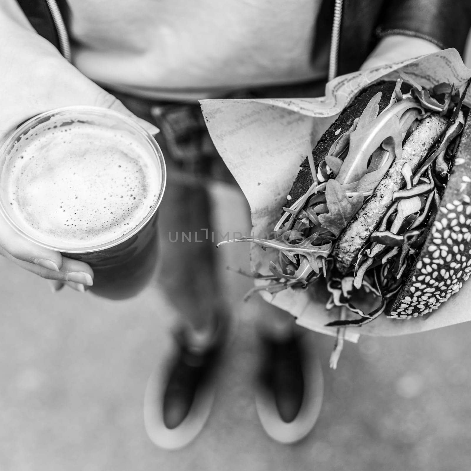 Close Up Of Woman Hands Holding Delicious Organic Salmon Vegetarian Burger and Homebrewed IPA Beer on Open Air Beer an Burger UrbanStreet Food Festival. Black and white image.