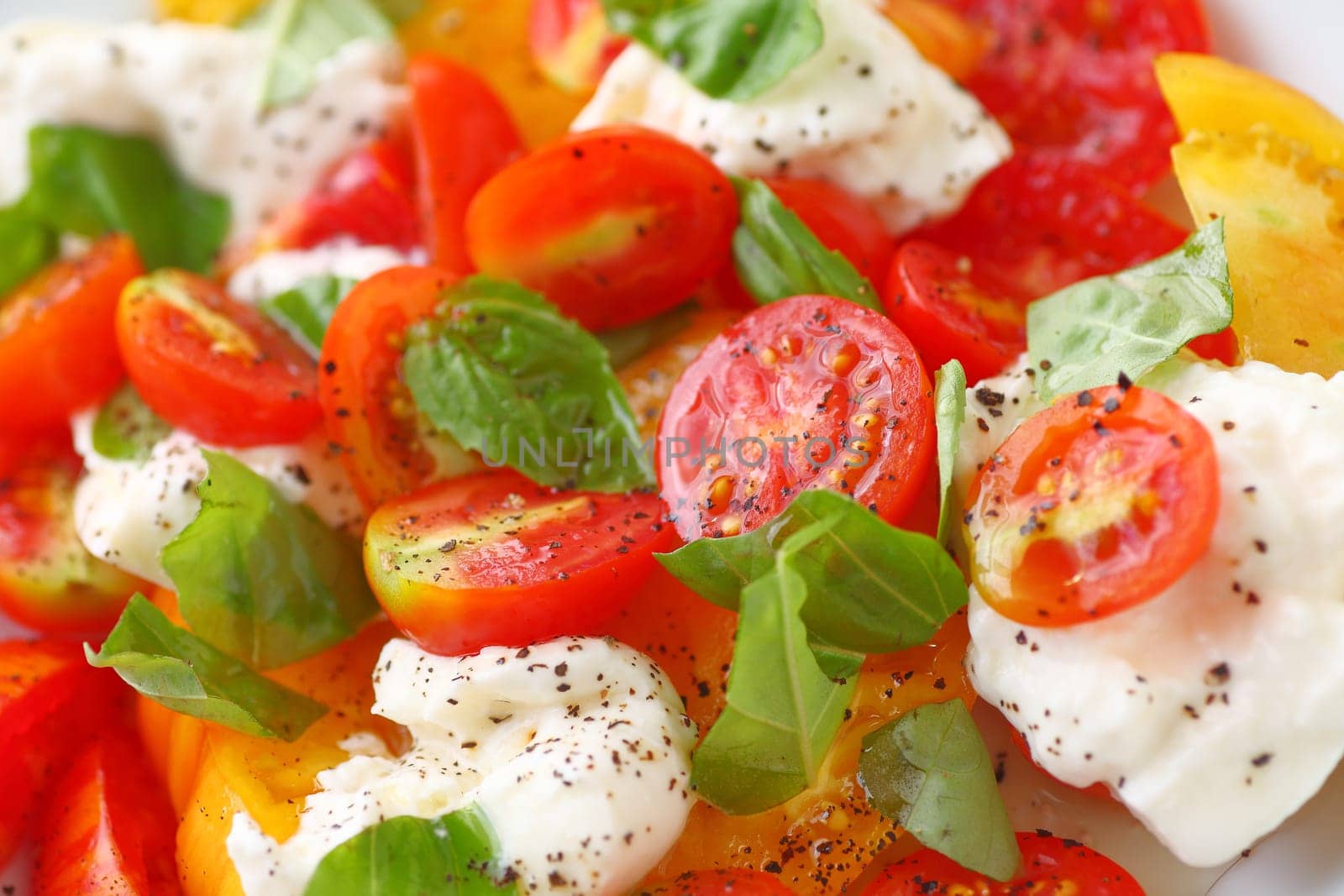 Cherry tomatoes, fresh basil, burrata cheese and black pepper in a fresh summer salad