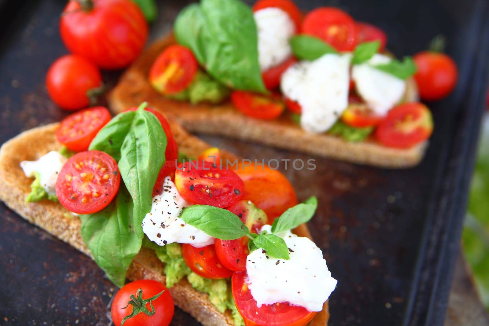 Cherry tomatoes, fresh basil and black pepper on avocado toast
