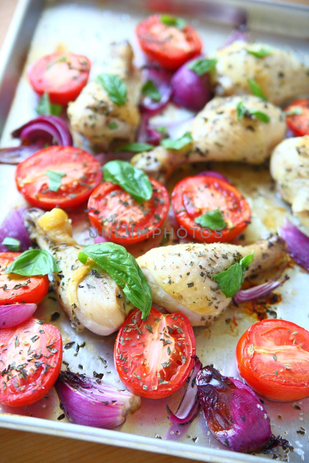 Chicken legs roasted with Roma tomatoes and red onions garnished with fresh basil leaves