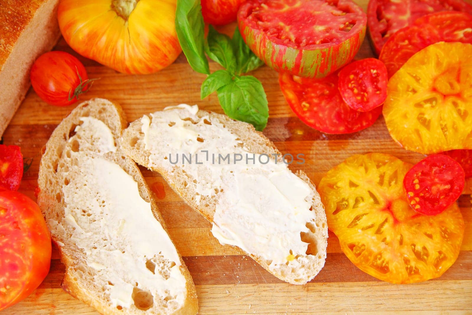 Bread slices with mayonnaise, sliced heirloom tomatoes and basil leaves on a cutting board