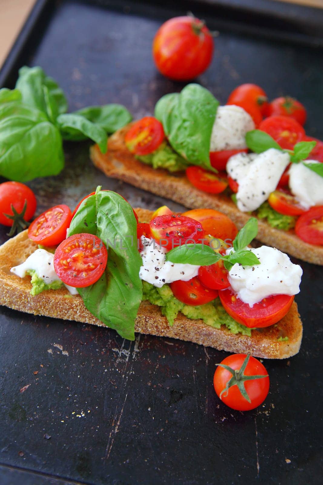 Closeup of toast spread with avocado, topped with burrata cheese, basil and cherry tomatoes